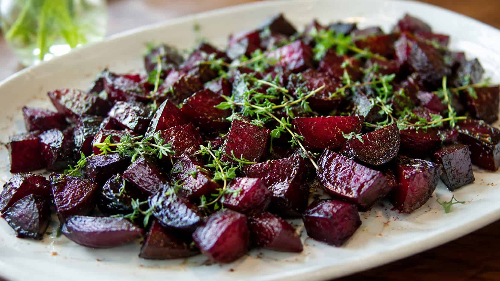 glossy balsamic roasted beet cubes spread wide across a serving plate, a scattering of fresh herbs on top, warm natural light, shallow depth of field, landscape orientation