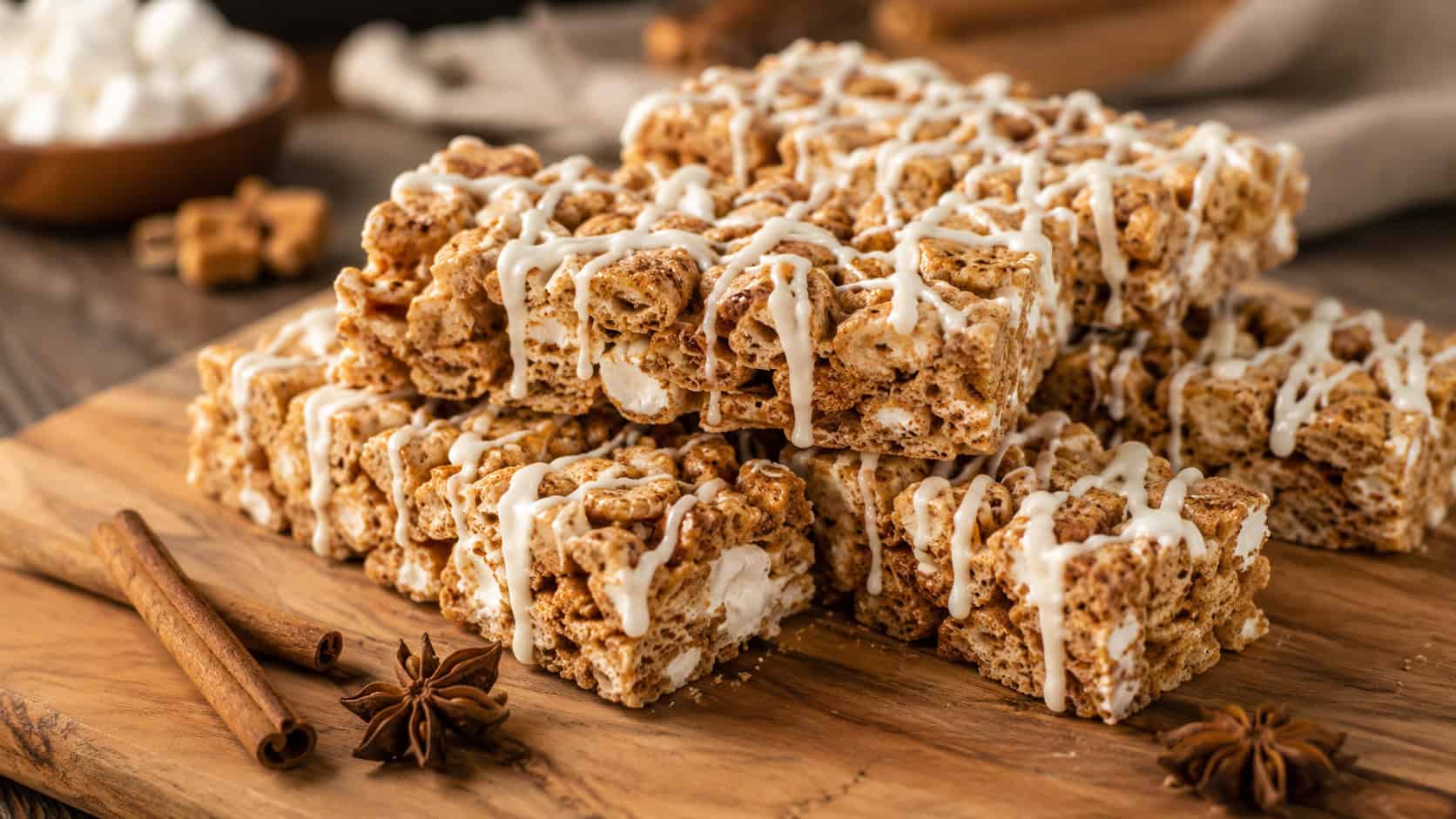 spiced gingerbread marshmallow cereal bars drizzled with white icing, in a wide horizontal shot stacked on a wooden cutting board with cinnamon sticks and star anise nearby, warm natural light, shallow depth of field, landscape orientation