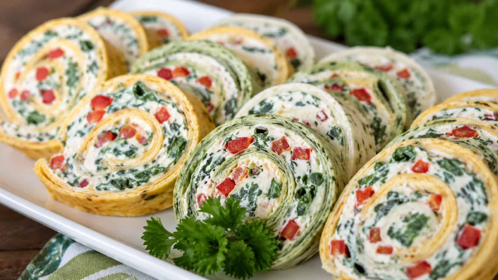 colorful tortilla pinwheels with creamy filling flecked with green spinach and red pepper, in a wide horizontal shot fanned across a white platter with a sprig of parsley, bright natural light, shallow depth of field, landscape orientation