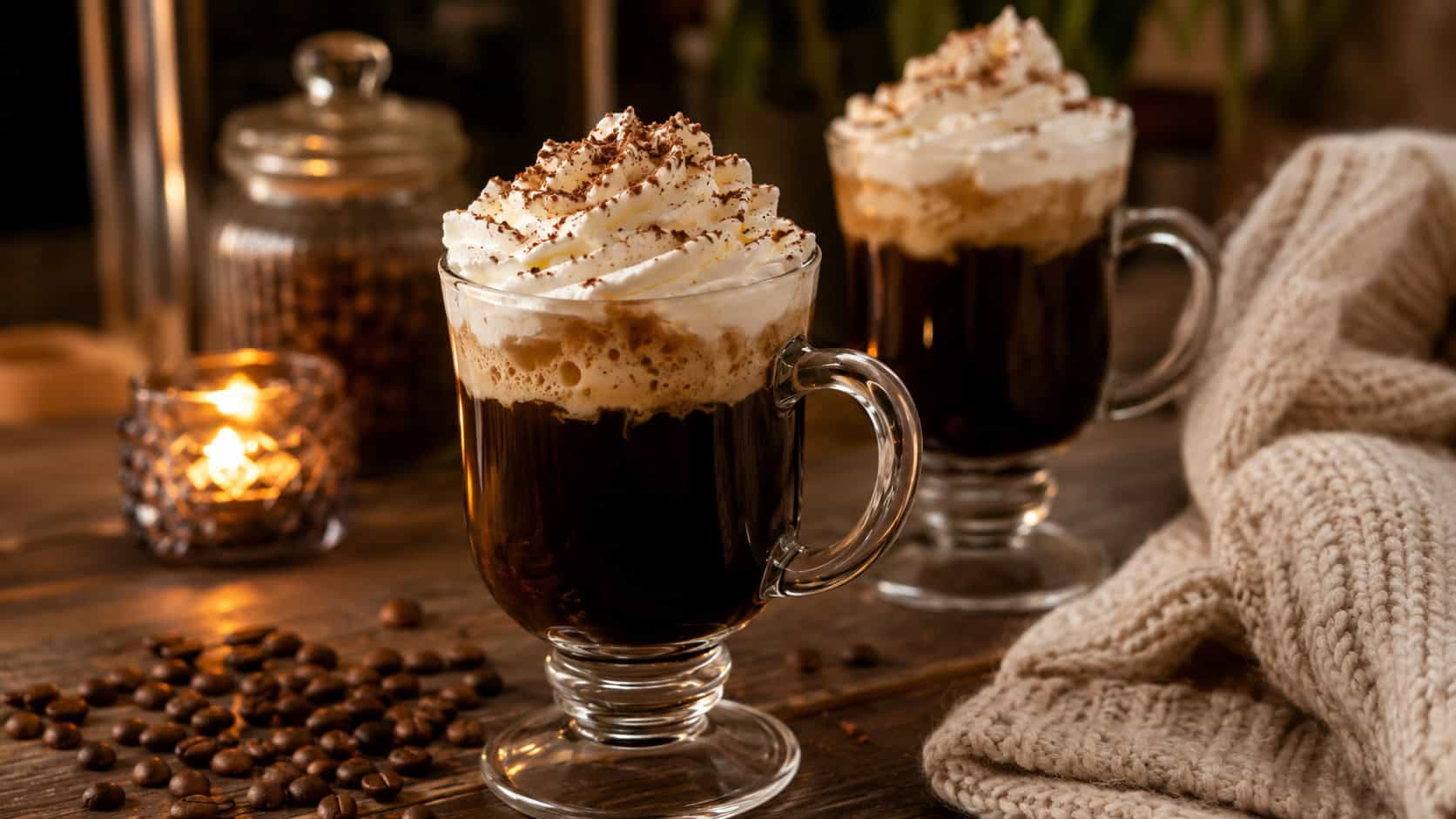 hazelnut Irish coffees topped with whipped cream in clear glass mugs arranged in a wide horizontal shot on a cozy table, coffee beans and a soft blanket nearby, warm candlelight, shallow depth of field, landscape orientation
