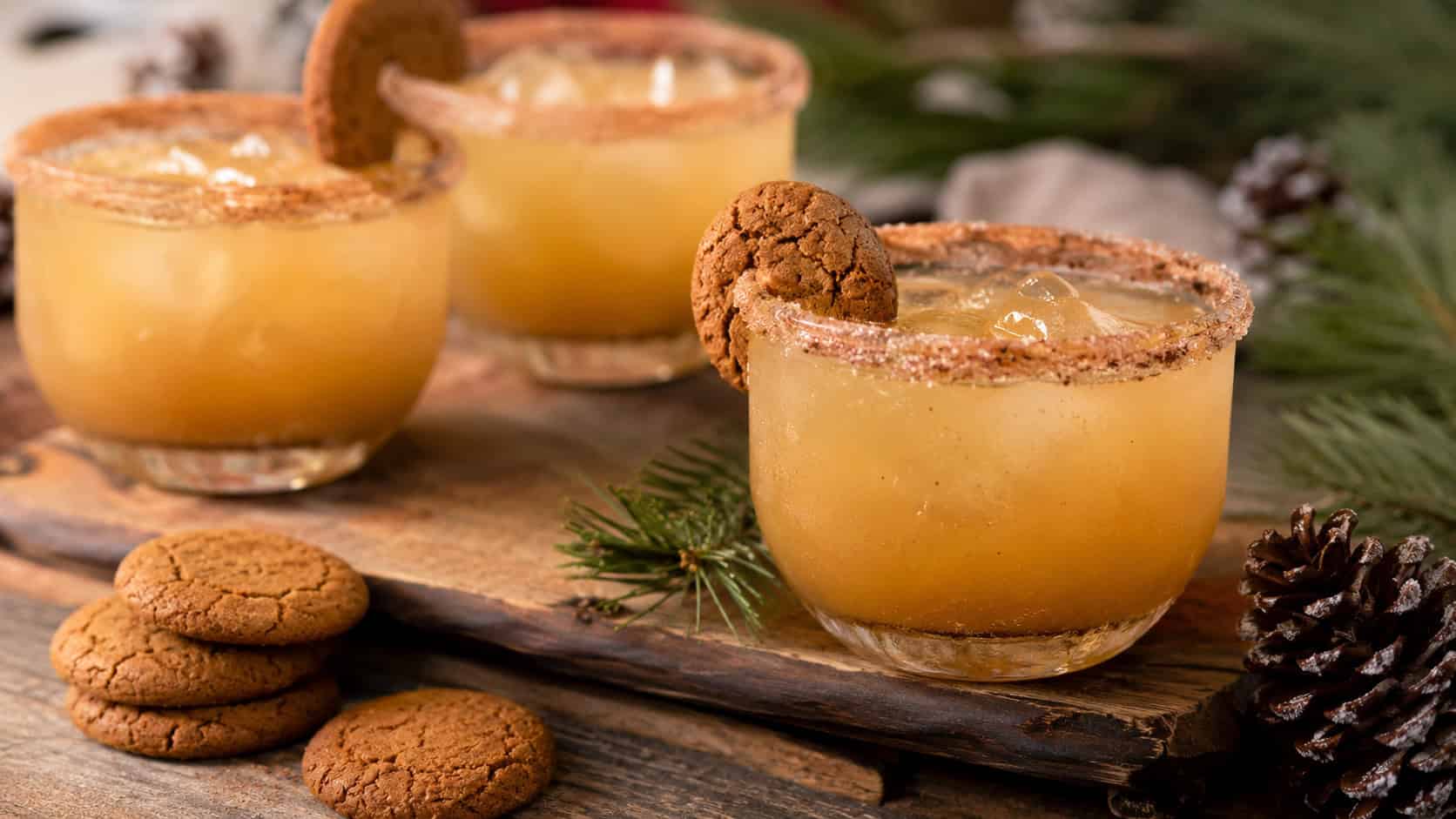 spiced ginger snap cocktails with cinnamon sugar rims arranged in a wide horizontal shot on a rustic table, ginger cookies and pine sprigs nearby, warm natural light, shallow depth of field, landscape orientation
