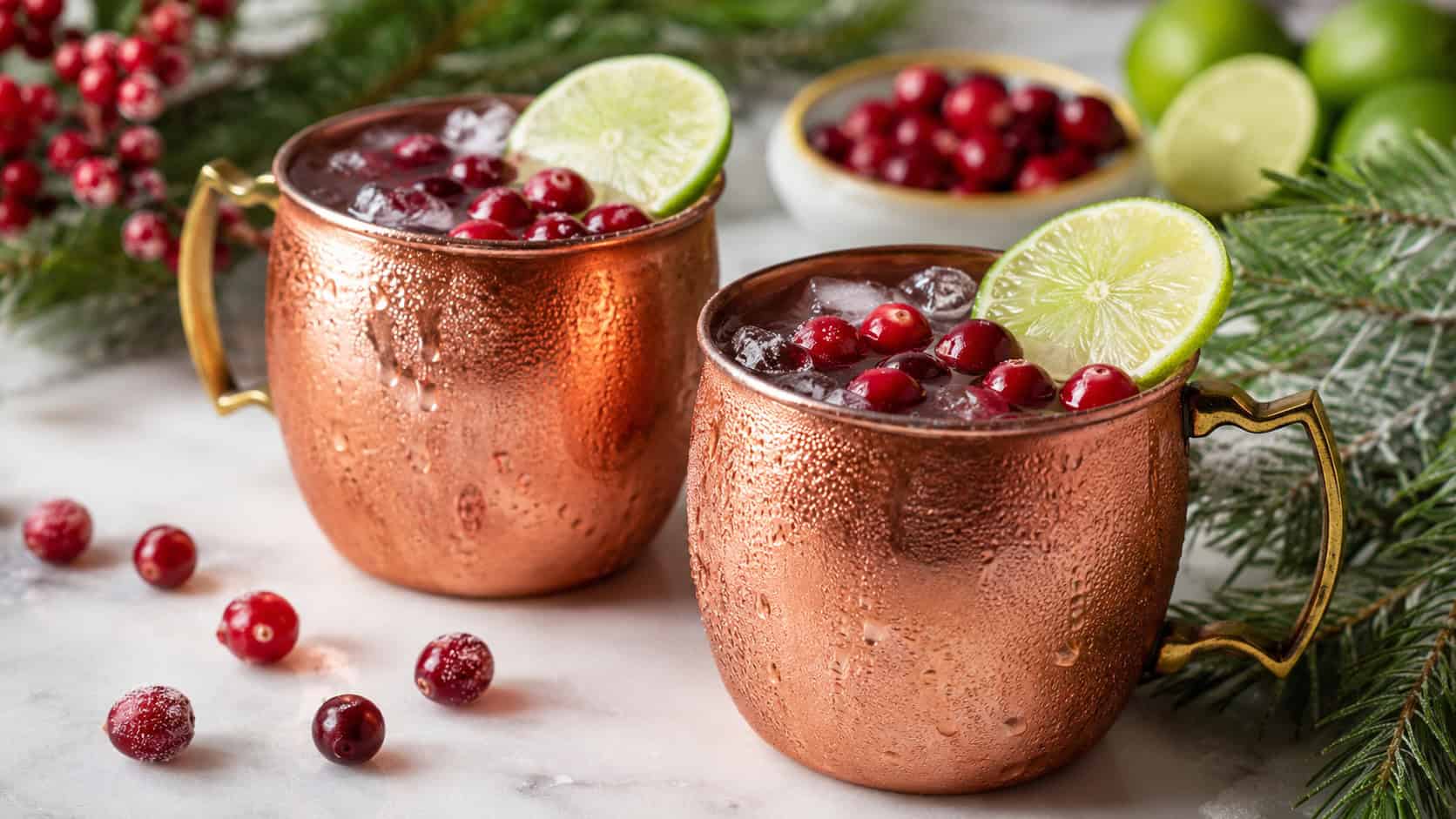 cranberry Moscow mules in copper mugs garnished with fresh cranberries and lime wheels arranged in a wide horizontal shot on a festive table, frost on the mugs and pine sprigs nearby, bright natural light, shallow depth of field, landscape orientation