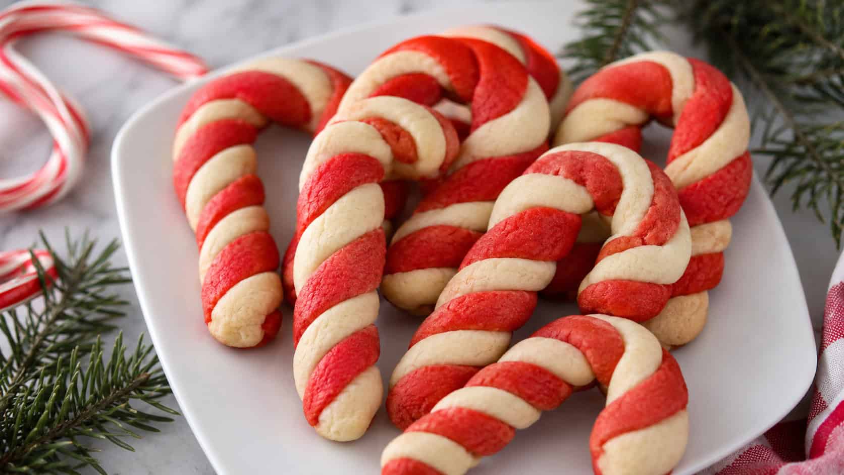 red and white twisted candy cane cookies arranged in a wide horizontal shot on a white plate, real candy canes and pine sprigs nearby, soft natural light, shallow depth of field, landscape orientation