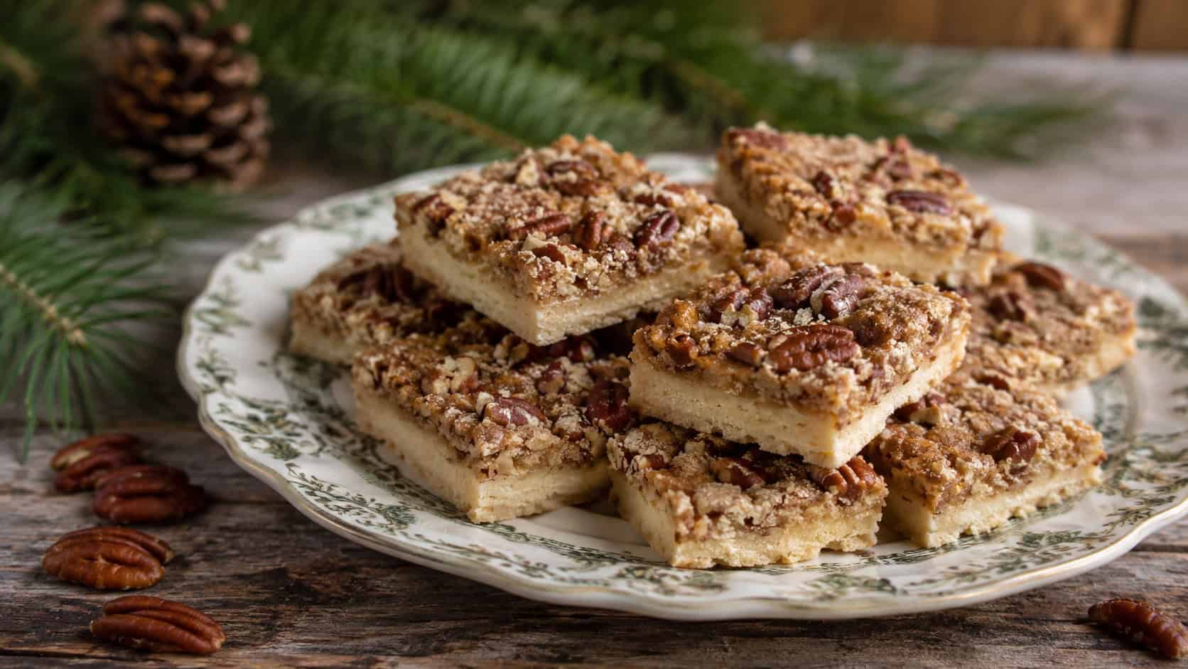 brown sugar pecan shortbread squares arranged in a wide horizontal shot on a vintage plate, scattered pecans and pine sprigs nearby, soft natural light, shallow depth of field, landscape orientation