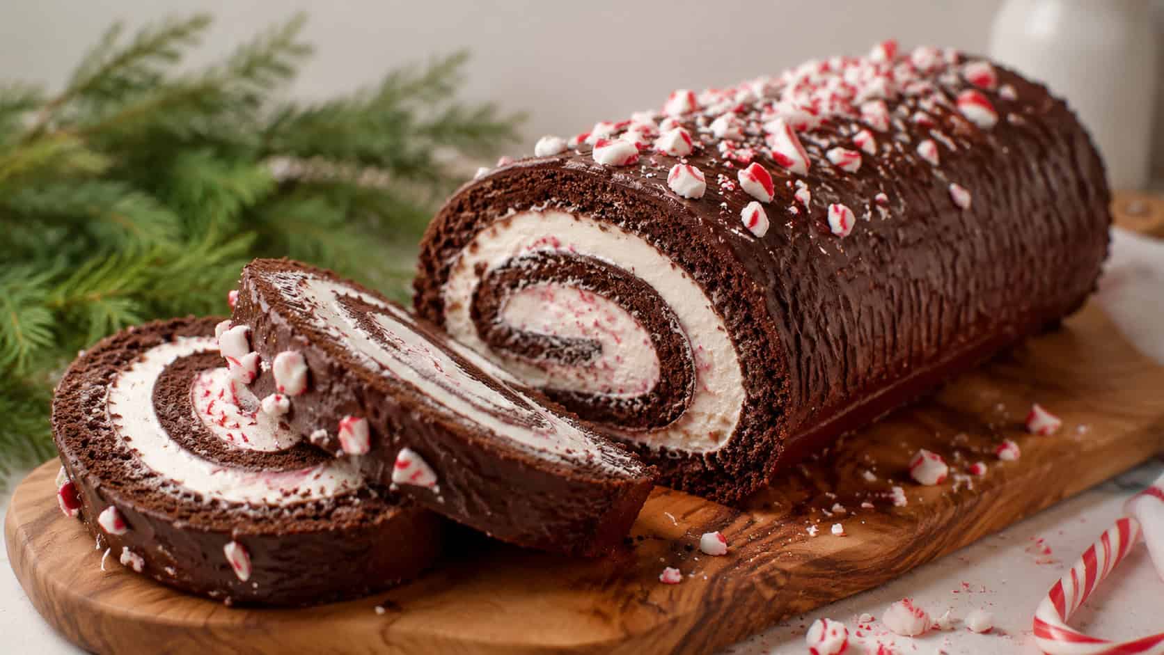 a sliced chocolate peppermint Swiss roll showing the cream spiral inside arranged in a wide horizontal shot on a serving board, crushed candy cane and greenery nearby, soft natural light, shallow depth of field, landscape orientation