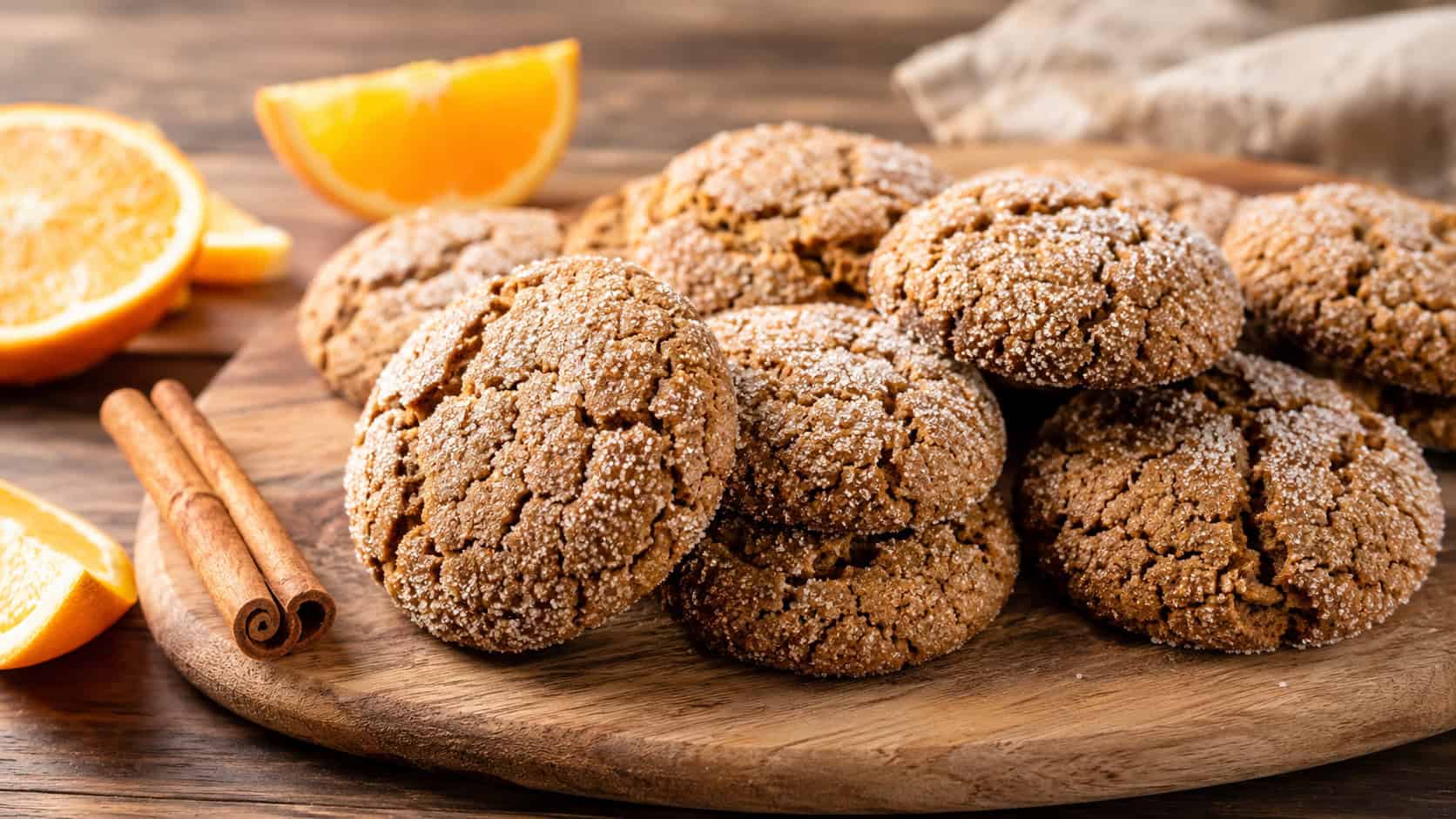 crackled orange molasses cookies rolled in sparkling sugar arranged in a wide horizontal shot on a wooden board, orange slices and cinnamon sticks nearby, warm natural light, shallow depth of field, landscape orientation