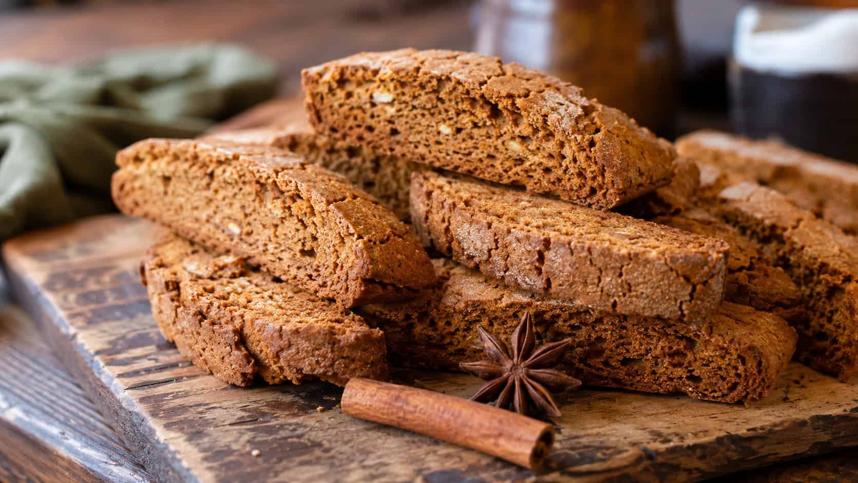 crisp gingerbread biscotti stacked wide across a rustic wooden board beside a cinnamon stick and star anise, warm natural light, shallow depth of field, horizontal landscape composition