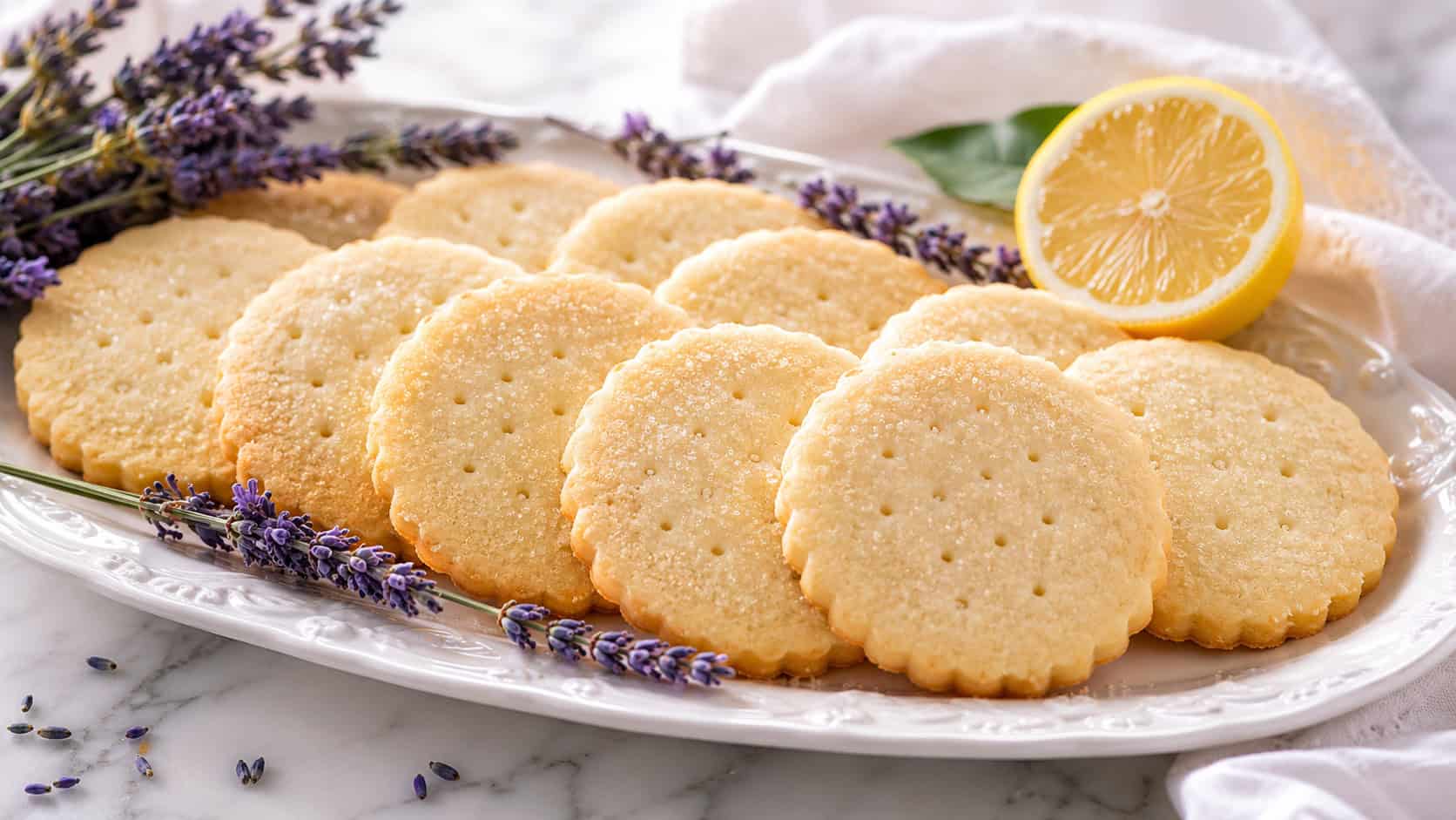 pale shortbread cookies arranged wide across a white platter, sprigs of lavender and a lemon half resting nearby, soft natural light, shallow depth of field, landscape orientation