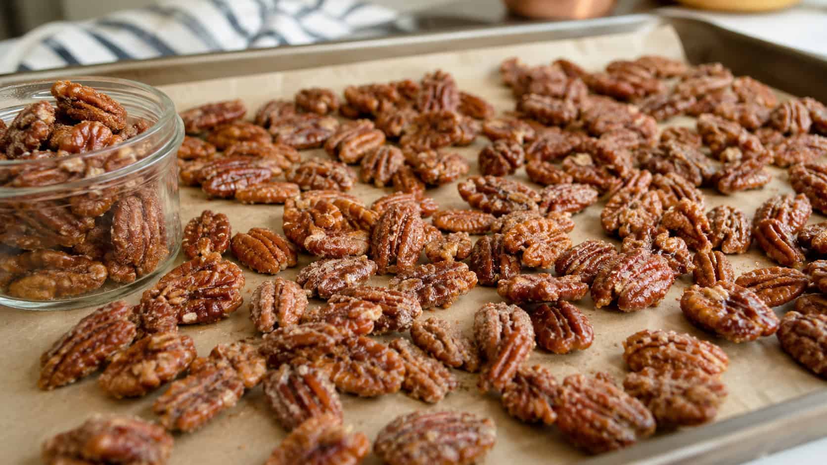 glossy cinnamon-sugar coated pecans spread wide across a parchment-lined tray, a few clustered in a small jar nearby, warm natural light, shallow depth of field, horizontal landscape composition