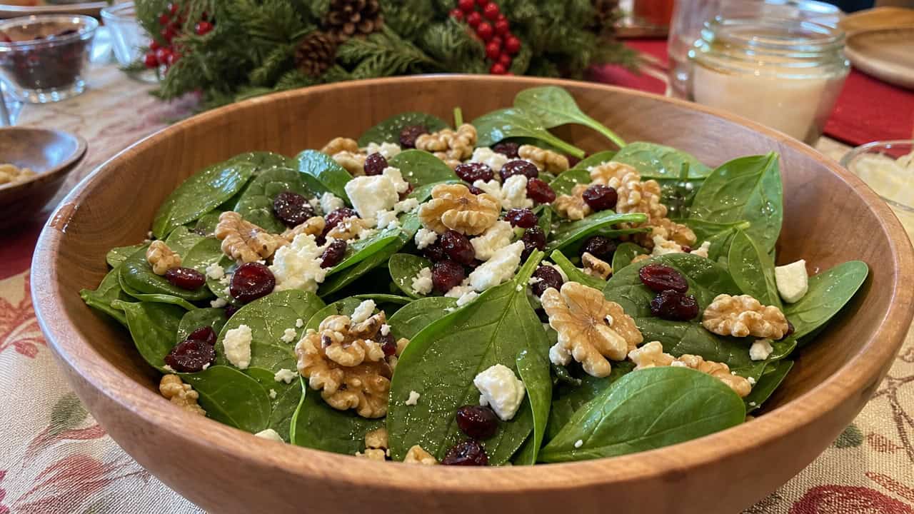 a fresh spinach salad with red dried cranberries, toasted walnuts, and crumbled white feta in a wide horizontal shot, in a large wooden salad bowl on a festive table, natural light, shallow depth of field, landscape orientation