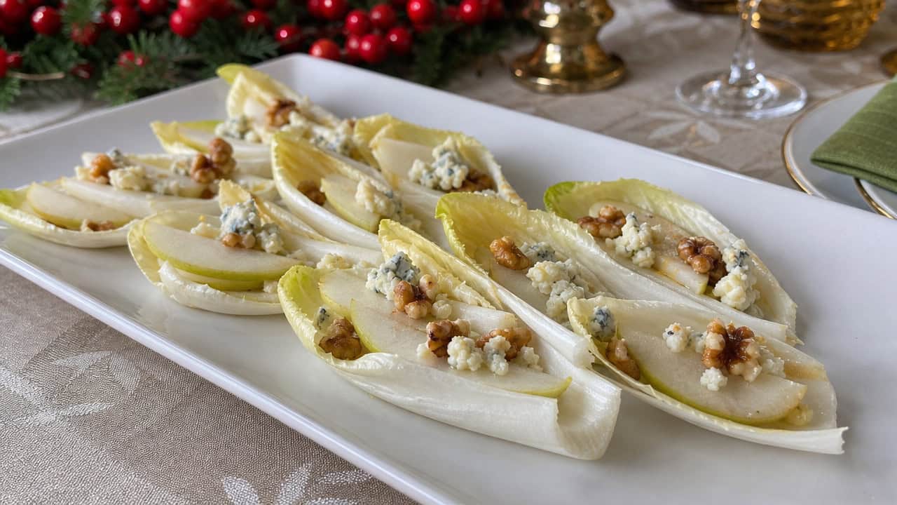 crisp pale endive leaves arranged like boats topped with pear slices, blue cheese crumbles, and toasted walnuts in a wide horizontal shot, on a white platter on a festive table, natural light, shallow depth of field, landscape orientation
