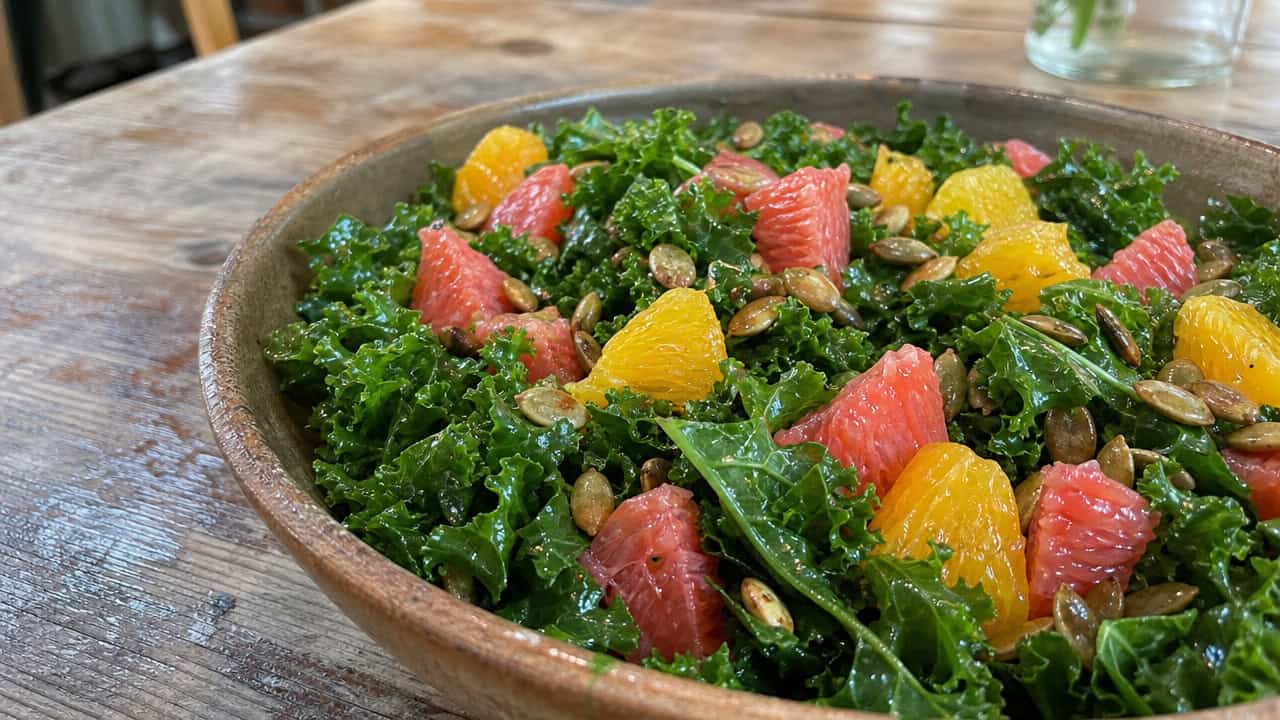 a hearty kale salad with bright orange and pink citrus segments and toasted pumpkin seeds in a wide horizontal shot, in a rustic bowl on a wooden table, natural light, shallow depth of field, landscape orientation