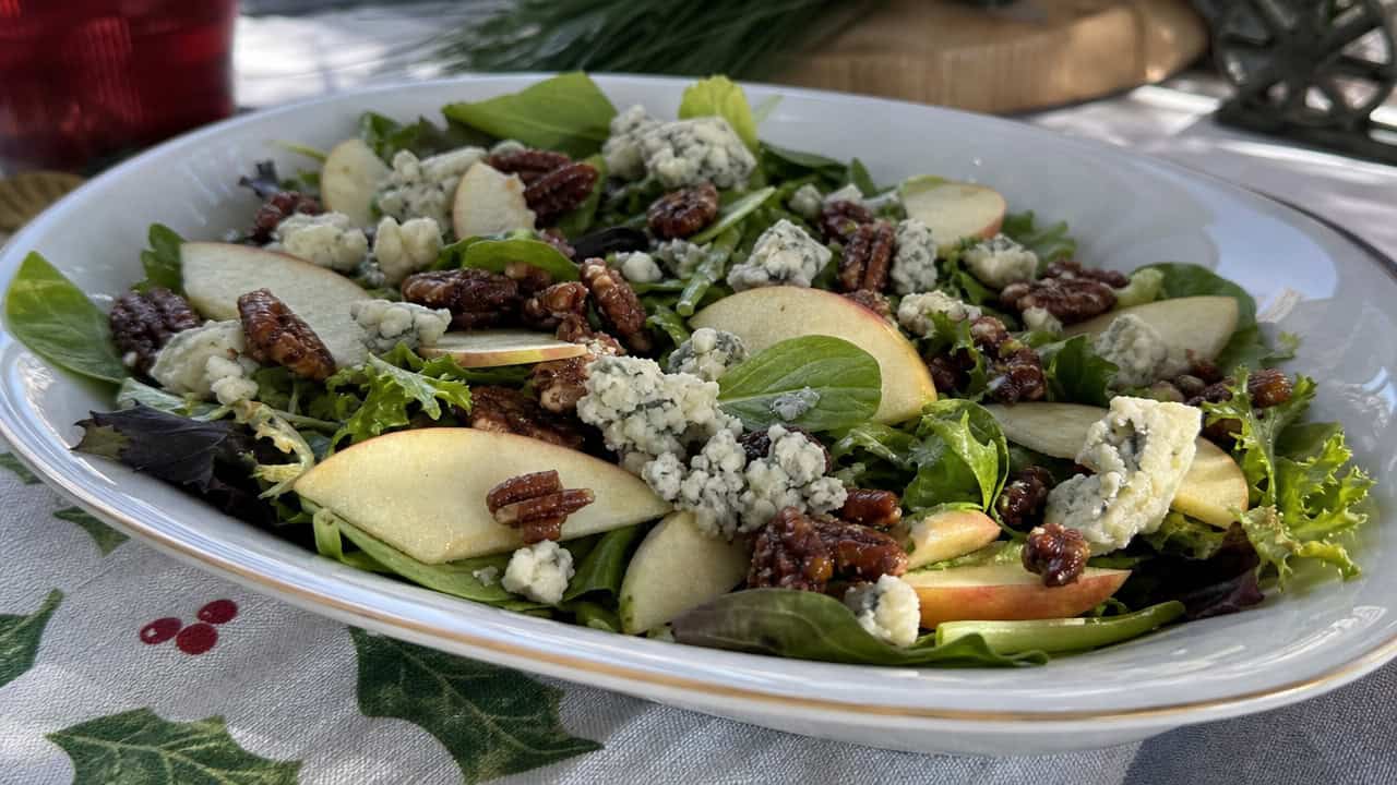 a fresh salad with thin apple slices, blue cheese crumbles, and candied pecans over greens in a wide horizontal shot, in a serving bowl on a festive table, natural light, shallow depth of field, landscape orientation