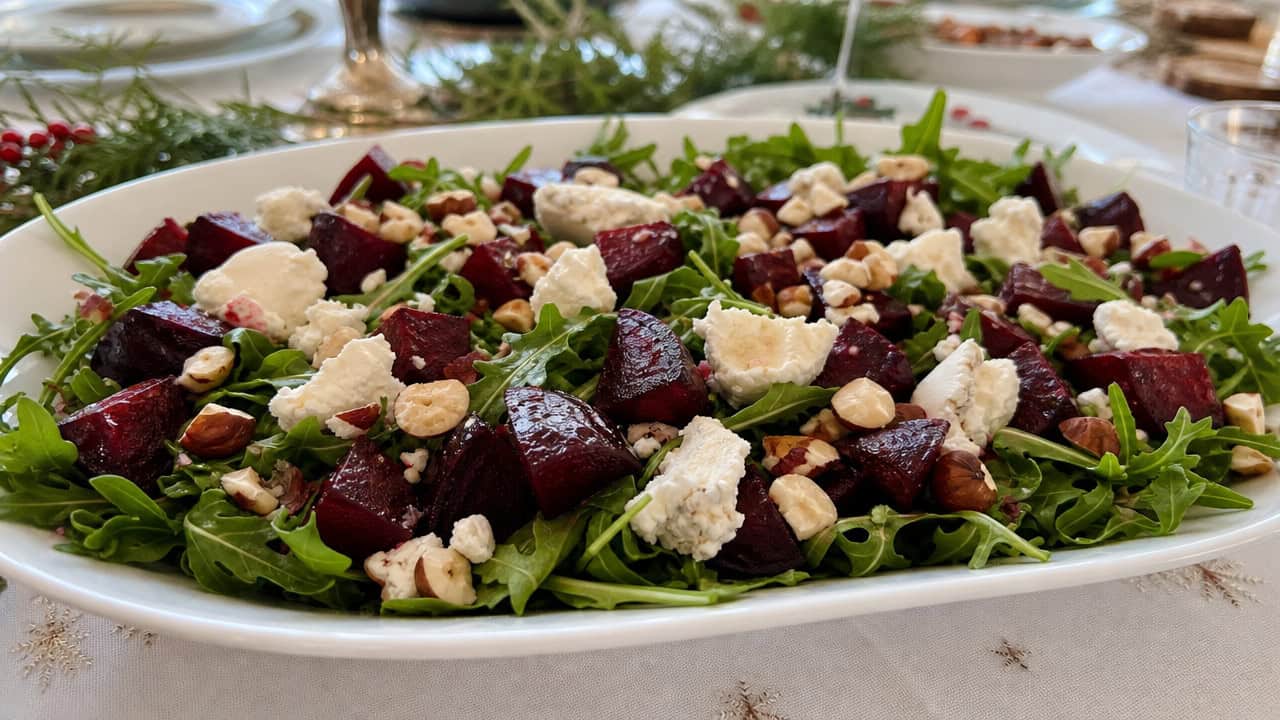 a vibrant salad with deep red roasted beet cubes, creamy white goat cheese, and chopped hazelnuts over arugula in a wide horizontal shot, on a white platter on a festive table, natural light, shallow depth of field, landscape orientation