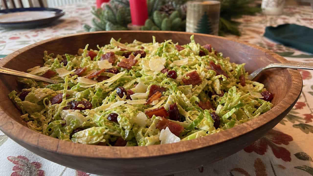 a shaved Brussels sprout salad with crispy bacon crumbles, shaved Parmesan, and red cranberries in a wide horizontal shot, in a wooden bowl on a holiday table, natural light, shallow depth of field, landscape orientation