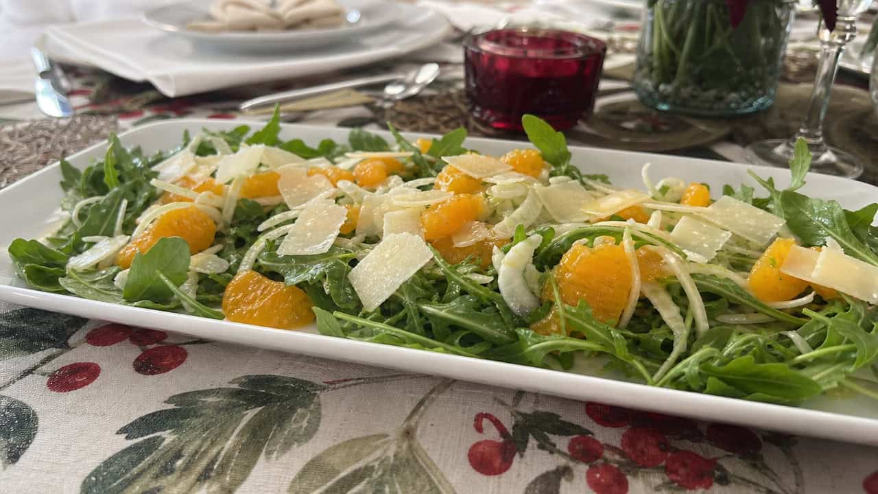 a light arugula salad with thinly shaved fennel and bright orange segments in a wide horizontal shot, shaved Parmesan on top, on a white platter on a festive table, natural light, shallow depth of field, landscape orientation