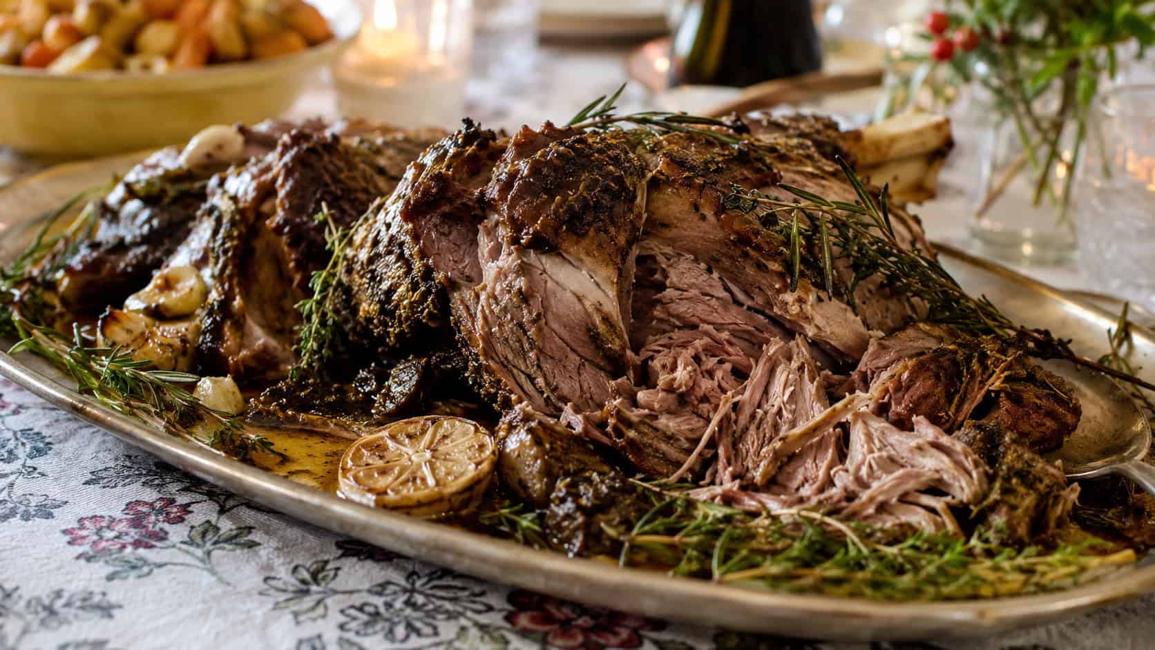 fall-apart Provencal herb lamb shoulder in a wide horizontal shot, pulled into chunks on a rustic platter with herbs and roasted garlic and pan juices on a country holiday table, natural light, shallow depth of field, landscape orientation