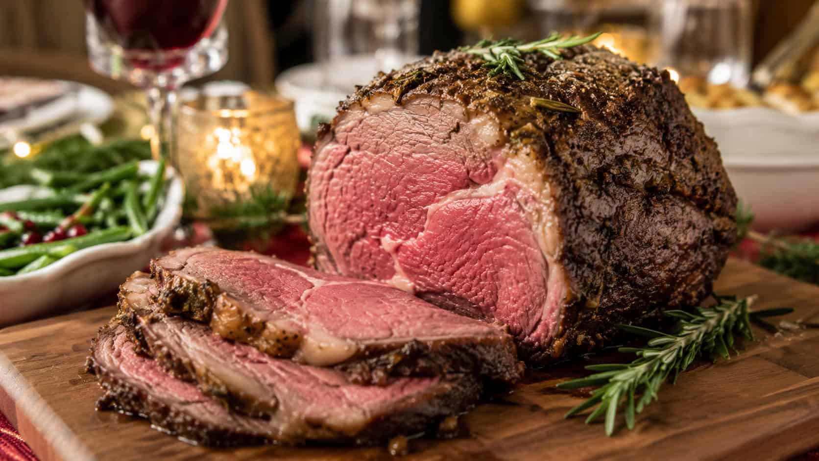a sliced prime rib roast on a wooden board in a wide horizontal shot, rosy pink center and herb-crusted edge, fresh rosemary garnish, on an elegant holiday table, warm natural light, shallow depth of field, landscape orientation