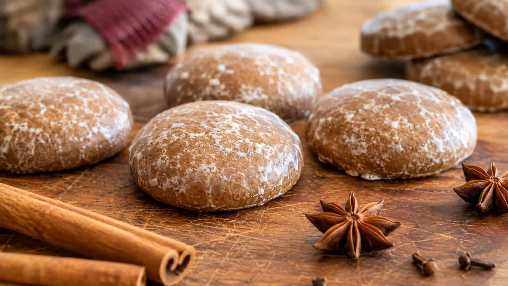 glazed round Lebkuchen spice cookies arranged in a wide horizontal shot on a wooden board, cinnamon sticks and star anise scattered nearby, warm natural light, shallow depth of field, landscape orientation