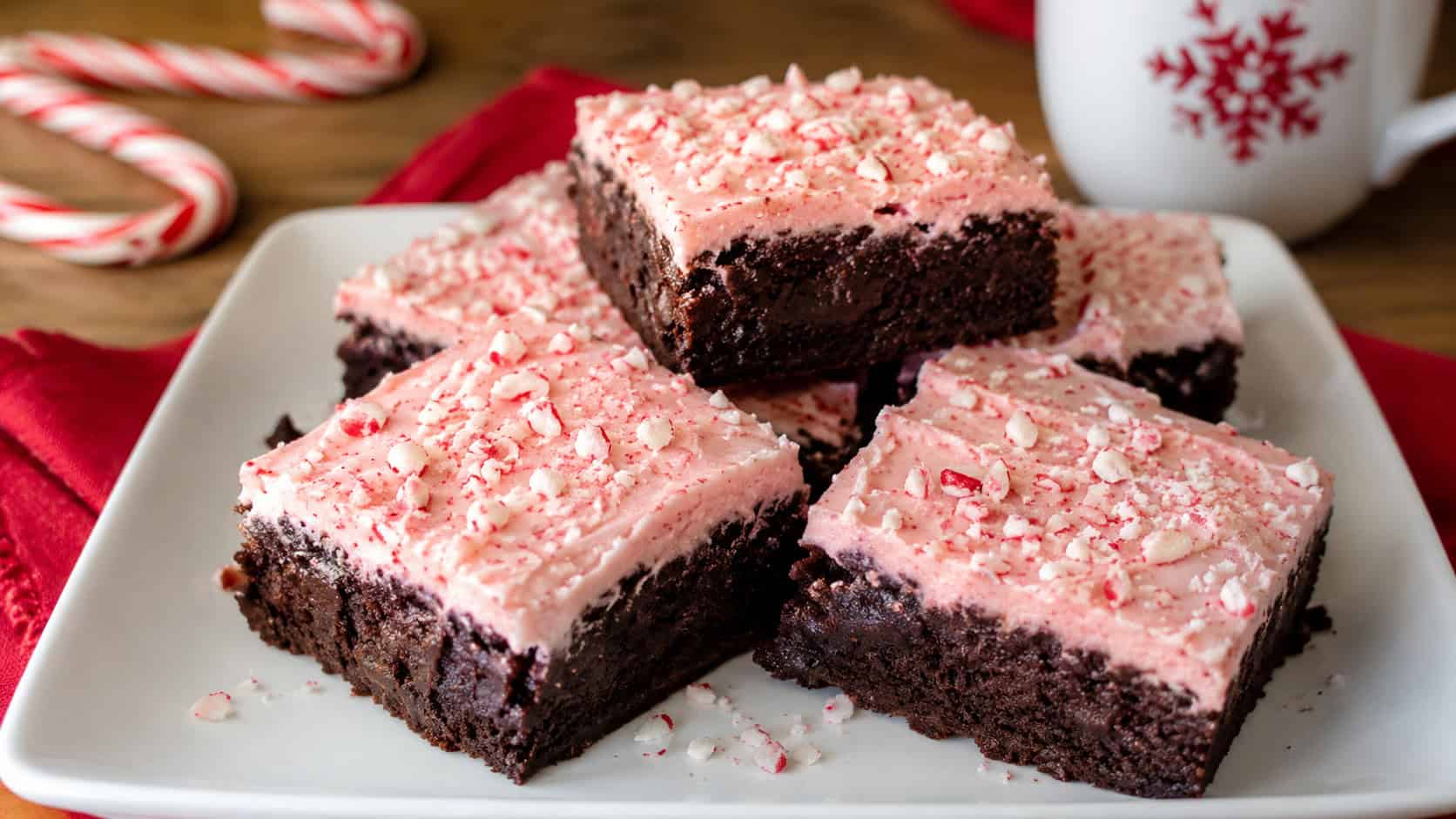 fudgy candy cane brownies with pink-tinted frosting and crushed peppermint arranged in a wide horizontal shot on a white plate, red linen and candy canes nearby, natural light, shallow depth of field, landscape orientation