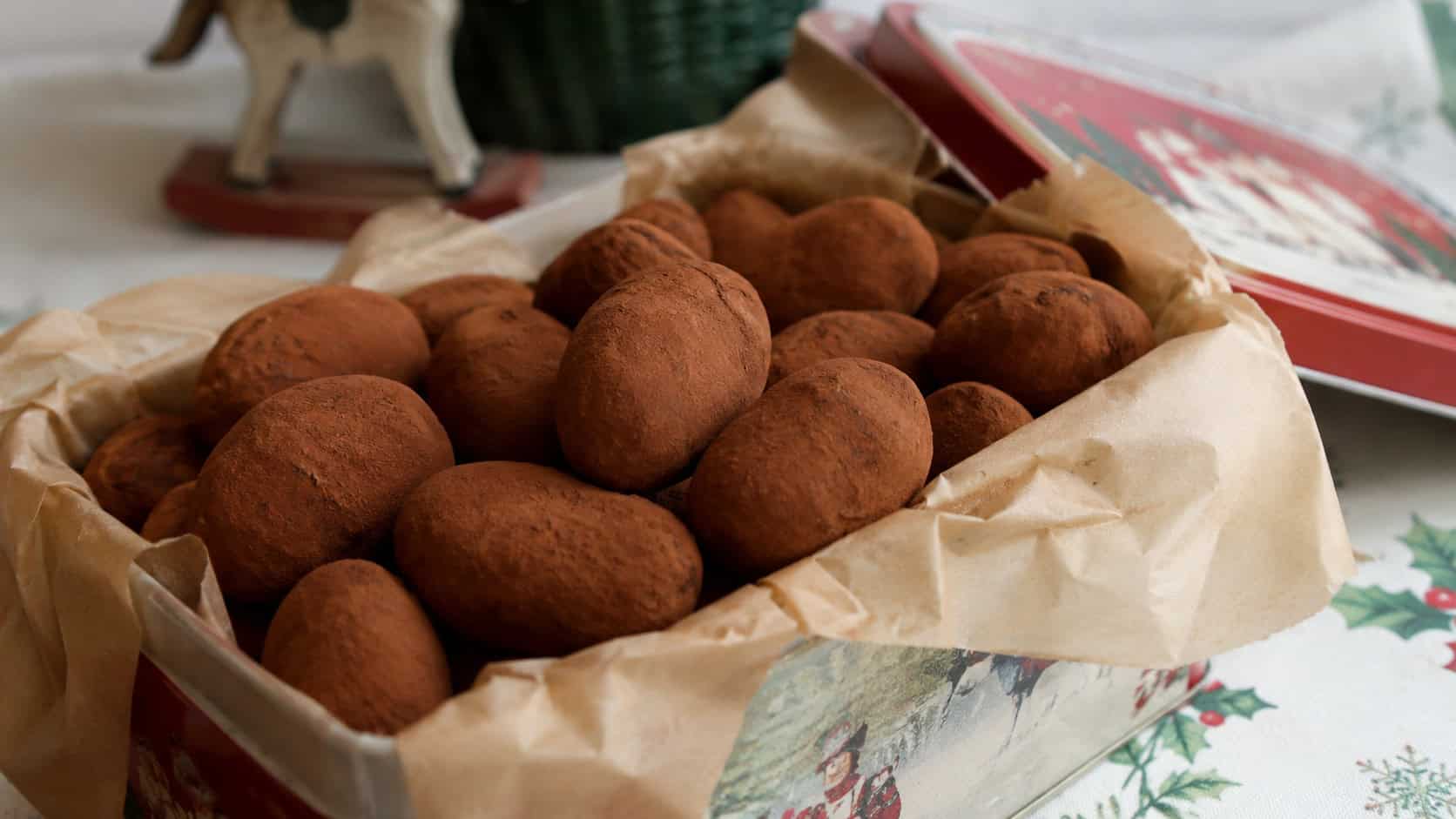 a pile of cocoa-dusted marzipan candies shaped like tiny potatoes, in a wide horizontal shot in a small tin lined with parchment on a holiday table, soft natural light, shallow depth of field, landscape orientation