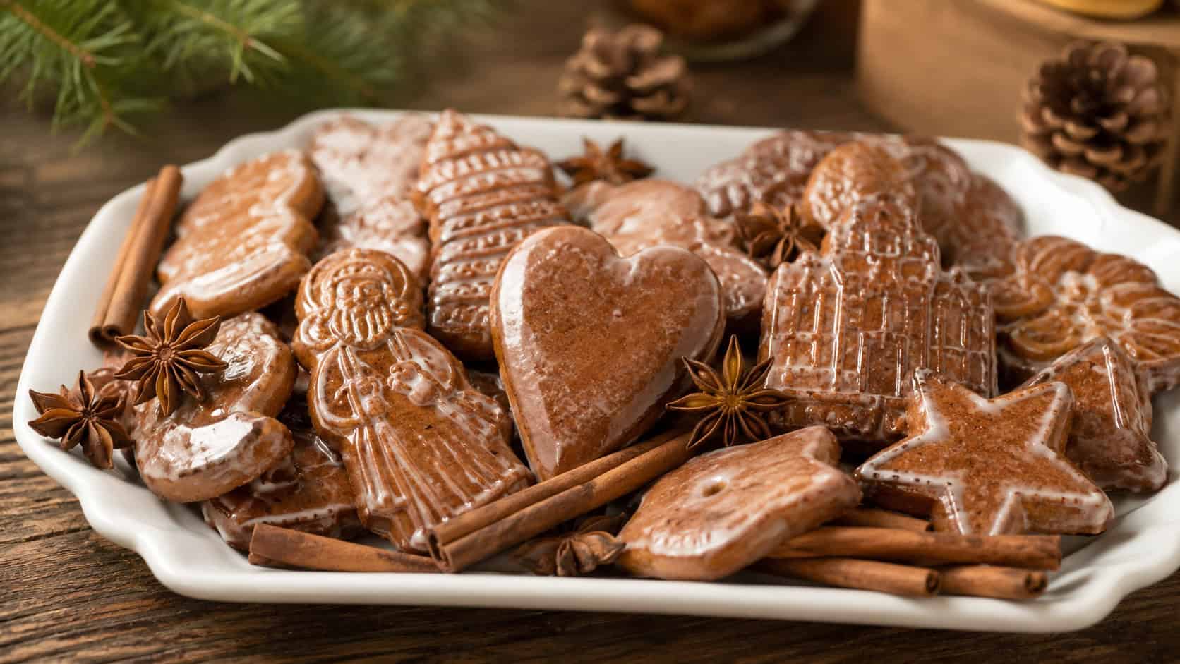 a batch of glossy glazed German gingerbread cookies arranged in a wide horizontal shot on a white ceramic platter with cinnamon sticks and star anise scattered around, warm natural light, shallow depth of field, landscape orientation