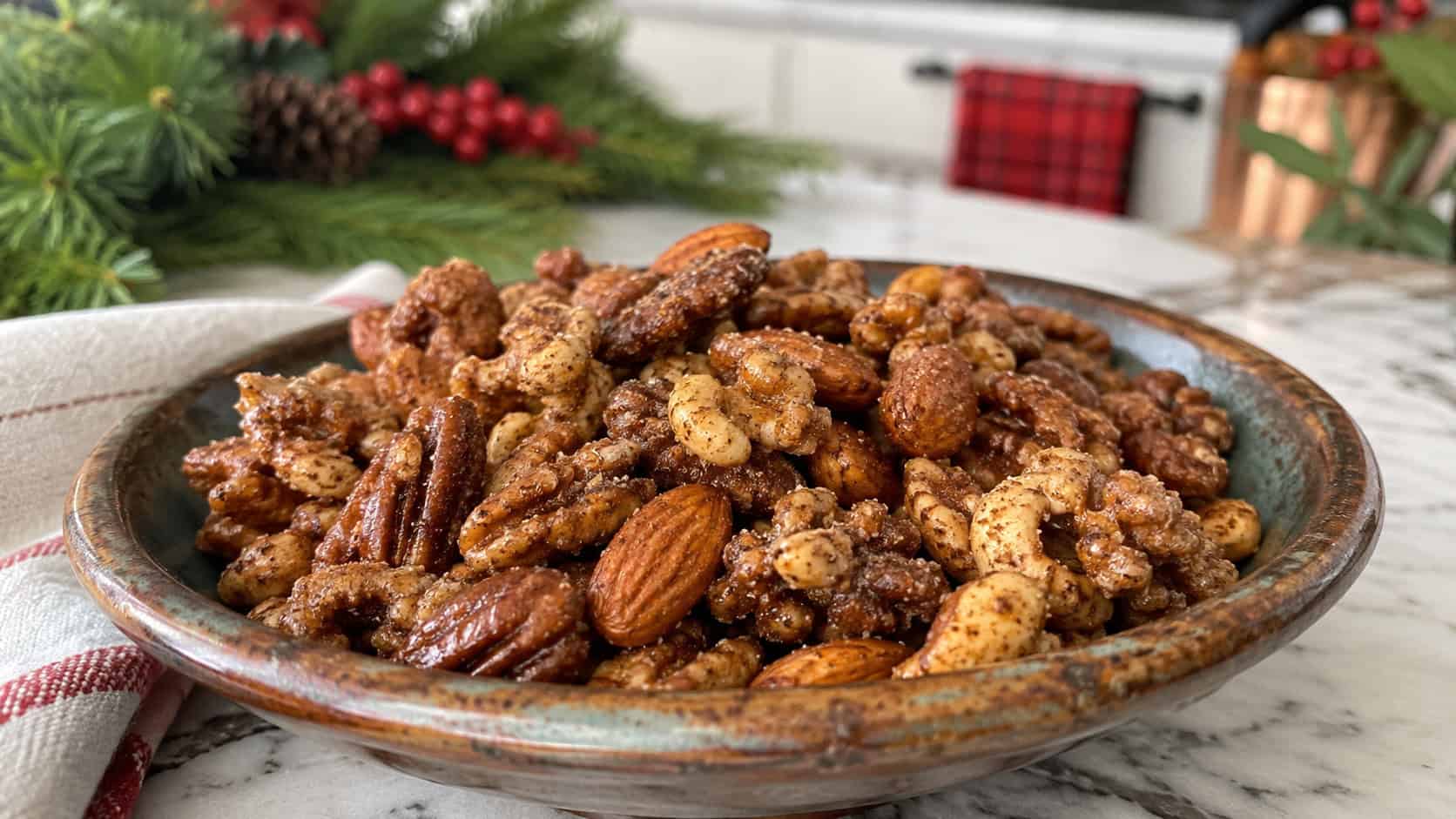 glossy spiced mixed nuts with a sugary cinnamon coating in a wide horizontal shot, served in a rustic bowl on a festive kitchen counter with greenery, natural light, shallow depth of field, landscape orientation