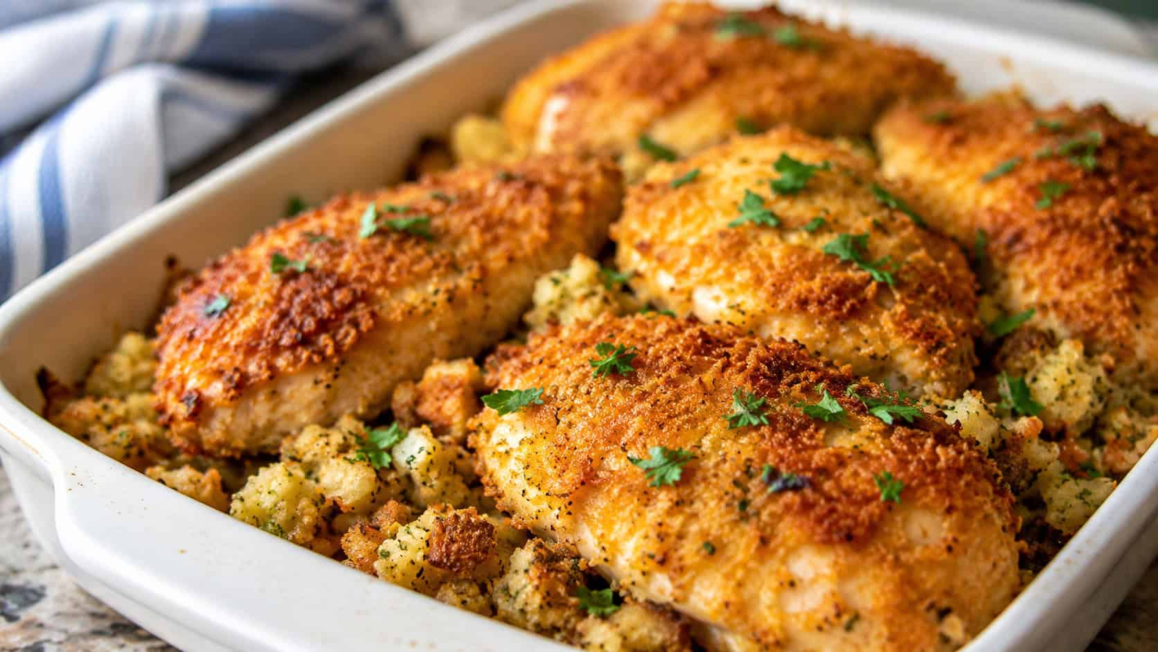 golden parmesan-crusted chicken resting over herbed stuffing in a baking dish, wide horizontal shot, crispy crumb texture, parsley garnish, natural kitchen light, shallow depth of field, landscape orientation