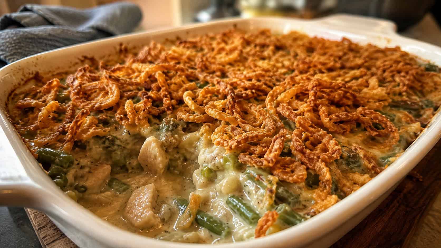 a chicken and green bean casserole in a baking dish in a wide horizontal shot, bubbling creamy sauce, golden crispy fried onion topping, a scoop pulled out, cozy kitchen light, shallow depth of field, landscape orientation