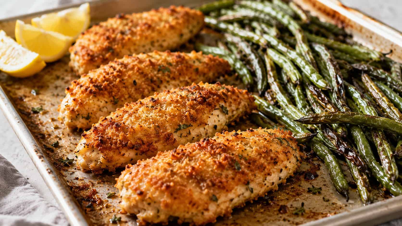 Parmesan crusted chicken and roasted green beans on a sheet pan in a wide horizontal shot, golden crunchy crust, blistered beans, lemon wedges in the corner, bright natural light, shallow depth of field, landscape orientation