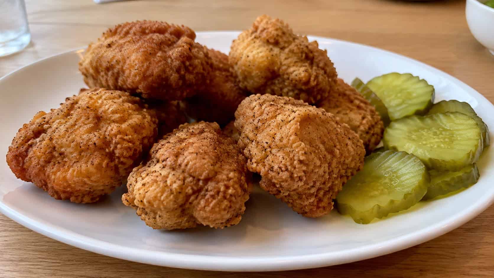 crispy buttermilk chicken nuggets in a wide horizontal shot on a white plate with a craggy golden crust and pickles, on a light wood table, natural daylight, shallow depth of field, landscape orientation