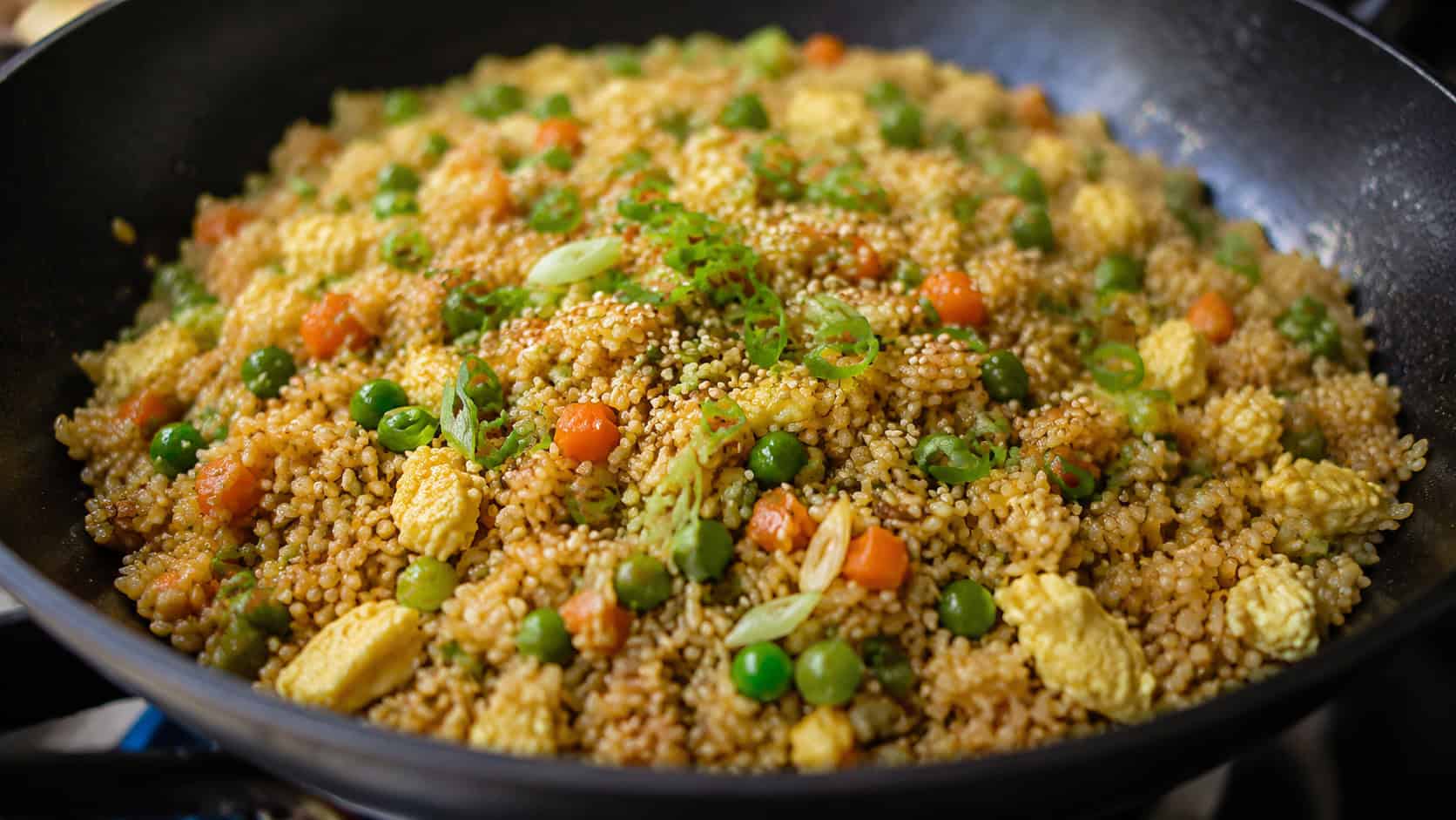 golden chicken fried rice with peas, carrots, and egg in a wok, garnished with sliced green onion and sesame seeds, wide horizontal shot, natural light, shallow depth of field, landscape orientation