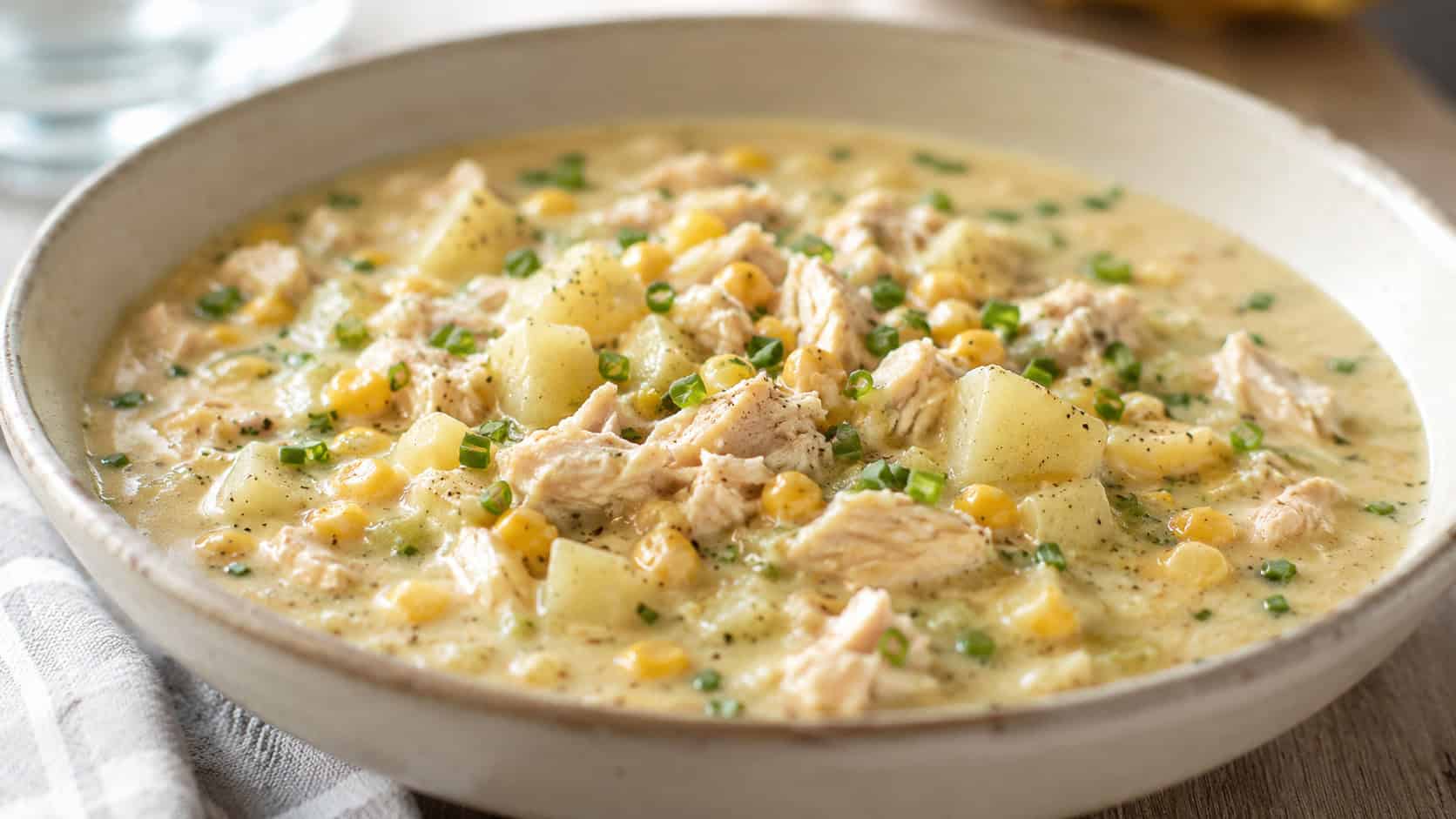 a wide horizontal bowl of chicken and corn chowder, thick creamy broth with golden corn and potatoes, fresh chives, natural light, shallow depth of field, landscape orientation