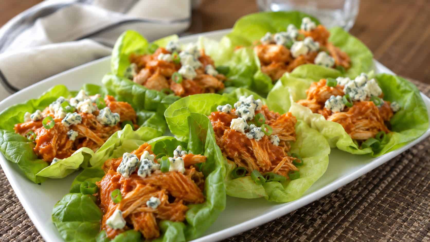 buffalo chicken lettuce wraps in crisp lettuce cups topped with blue cheese, arranged on a wide platter, set on a table, natural light, shallow depth of field, landscape orientation