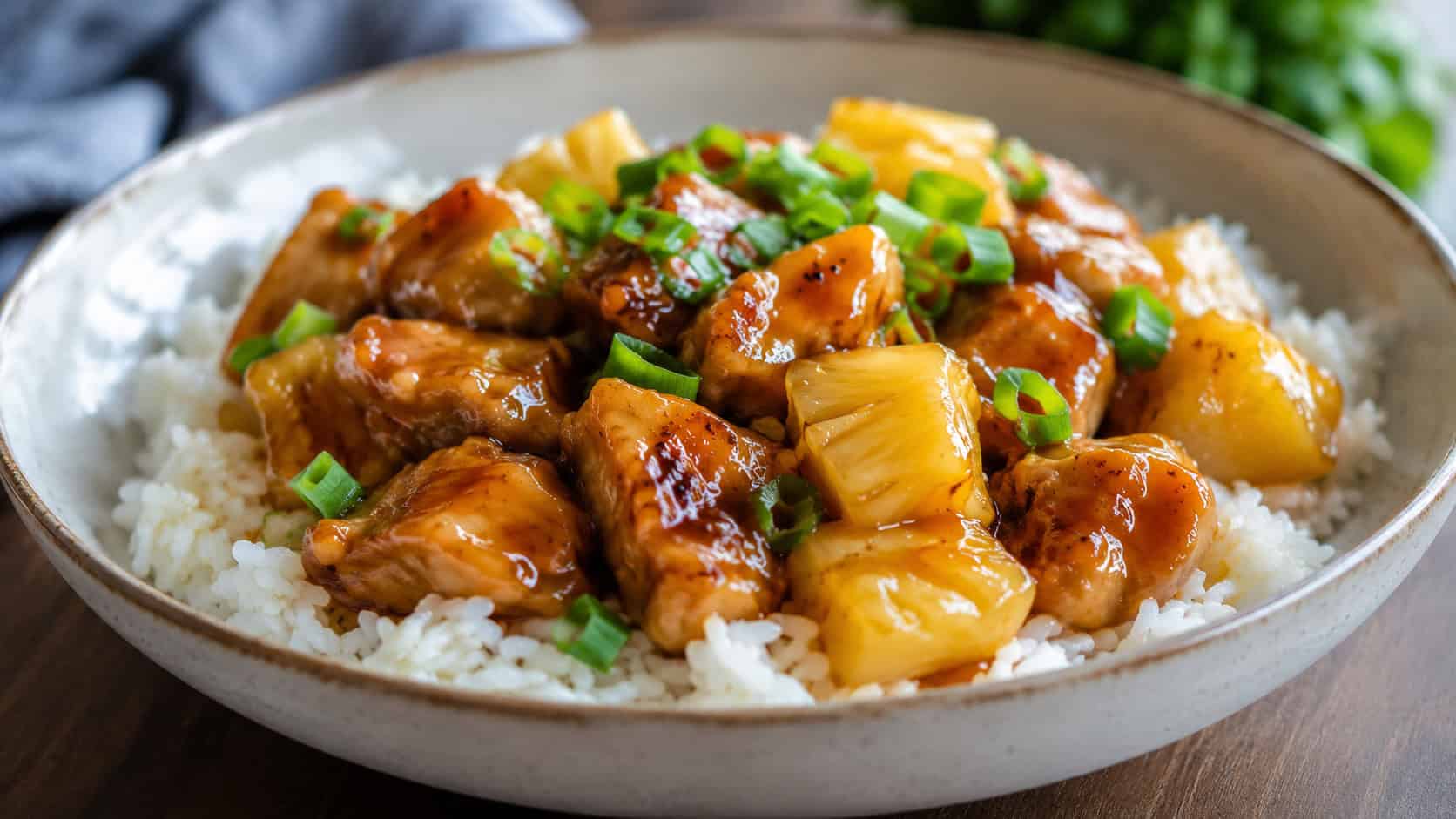 pineapple teriyaki chicken with glossy sauce and pineapple chunks over rice in a wide bowl with green onions, set on a table, natural light, shallow depth of field, landscape orientation