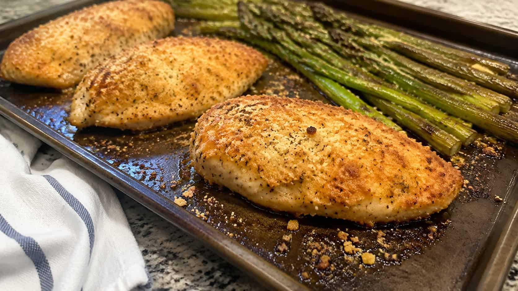 garlic parmesan chicken breasts with roasted green asparagus on a sheet pan, golden parmesan crust and bits of garlic, on a kitchen counter, wide horizontal shot, natural light, shallow depth of field, landscape orientation