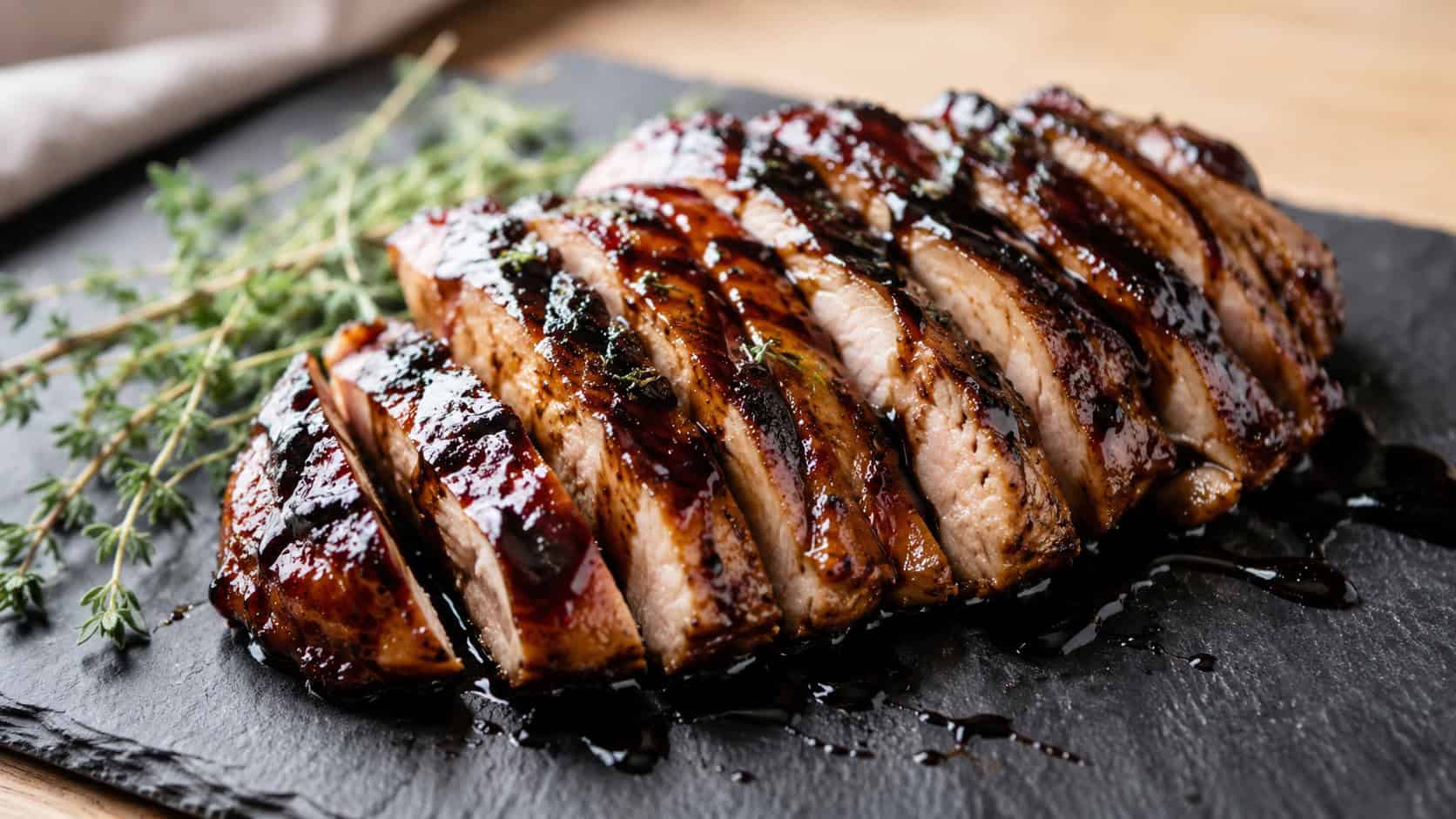 sliced balsamic glazed chicken breast with a dark glossy glaze drizzled over, fresh thyme sprigs alongside, on a slate serving board, wide horizontal shot, natural light, shallow depth of field, landscape orientation