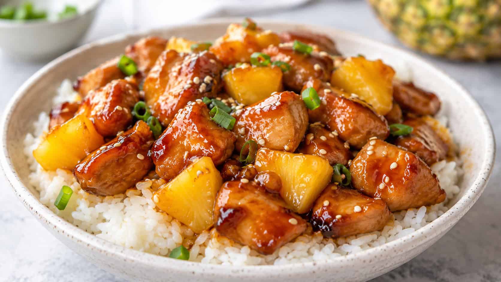 teriyaki pineapple chicken over rice in a wide horizontal frame on a bowl, glossy brown sauce with golden pineapple chunks and sesame seeds, bright clean light, shallow depth of field, landscape orientation