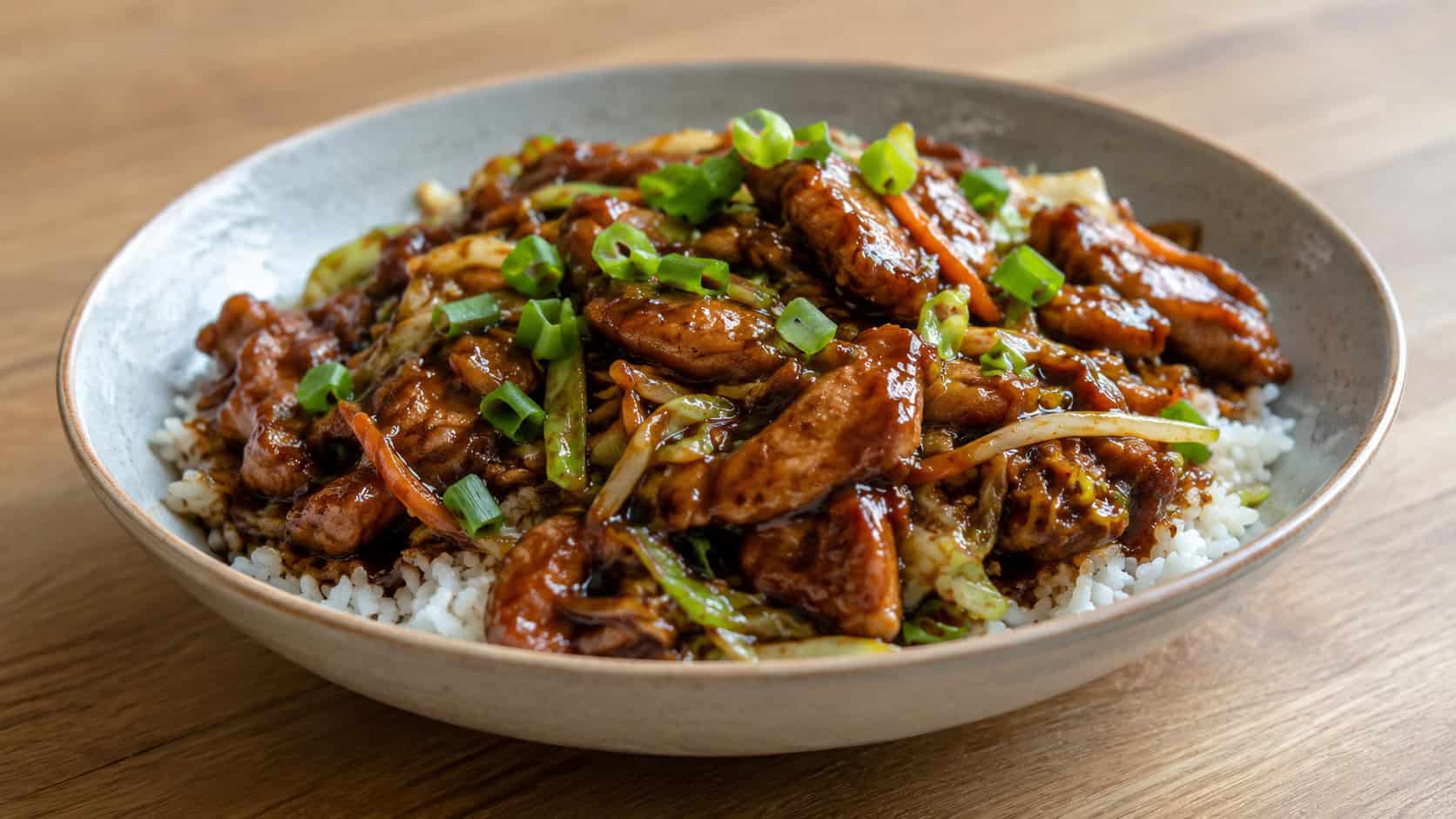 soy sauce chicken stir fry with shredded cabbage and carrot in a wide horizontal shot, glistening dark sauce, served in a simple bowl over rice, topped with green onion, on a plain wooden table, natural light, shallow depth of field, landscape orientation