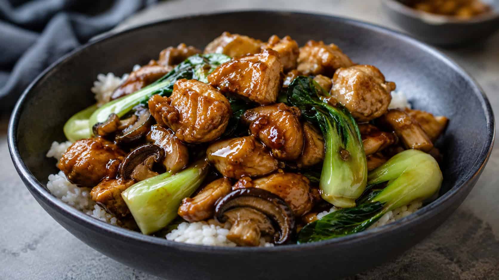 ginger soy chicken stir fry with baby bok choy and shiitake mushrooms in a wide horizontal shot, savory glossy sauce, served in a dark bowl over rice, on a stone table, natural light, shallow depth of field, landscape orientation
