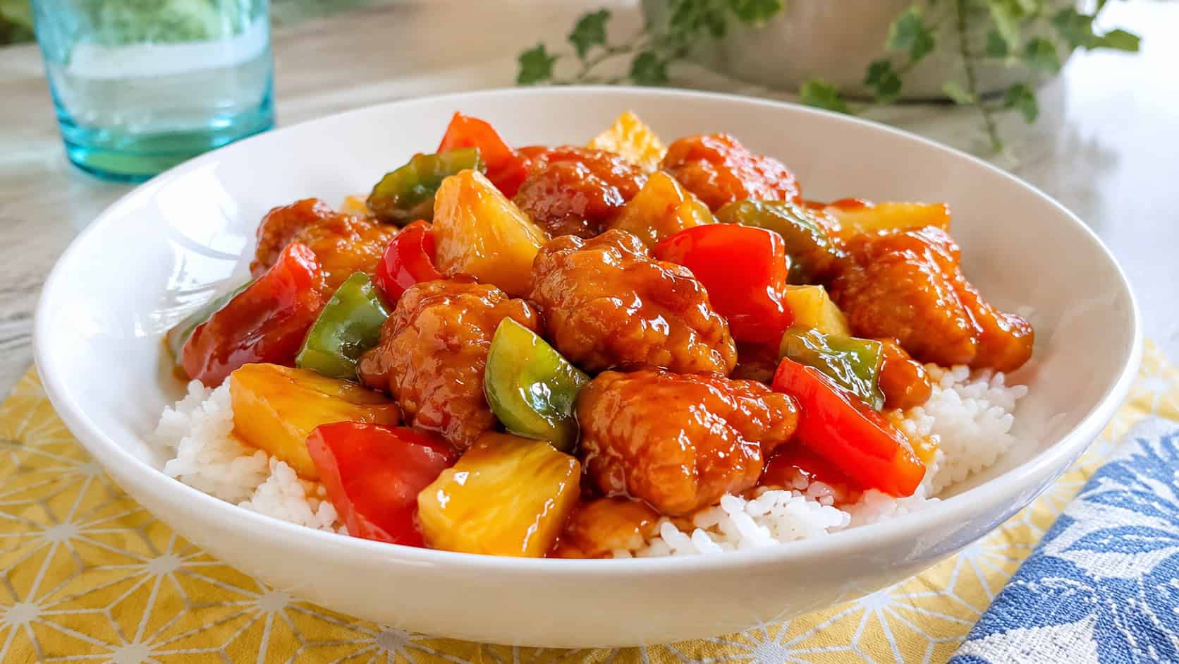sweet and sour chicken stir fry with pineapple and red and green peppers in a wide horizontal shot, glossy ruby-red sauce, served in a white bowl over rice, on a bright cheerful table, natural light, shallow depth of field, landscape orientation