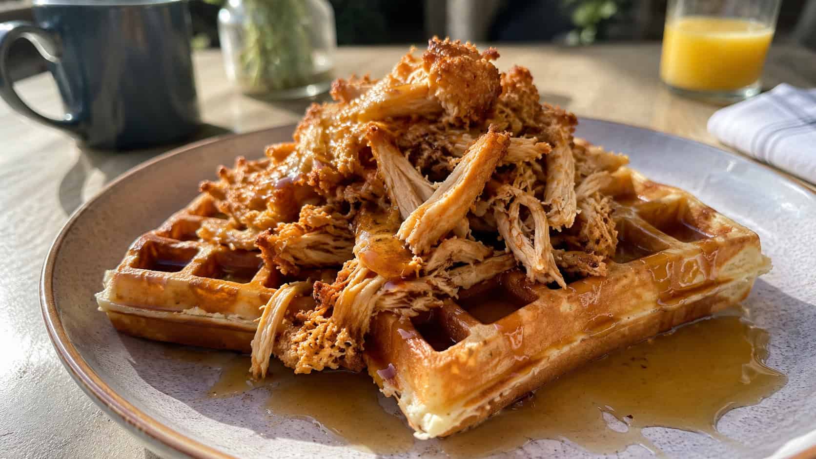 golden waffles topped with crispy shredded chicken and a maple syrup drizzle on a plate in a wide horizontal shot, syrup pooling on the side, sunny breakfast table, bright natural light, shallow depth of field, landscape orientation