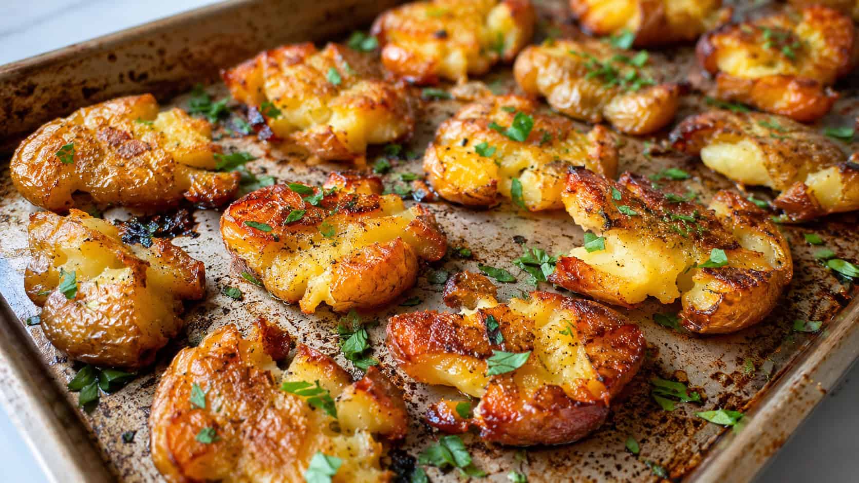 crispy smashed potatoes in a wide horizontal shot, golden and crackly-edged, sprinkled with fresh parsley on a rustic sheet pan, bright natural light, shallow depth of field, landscape orientation