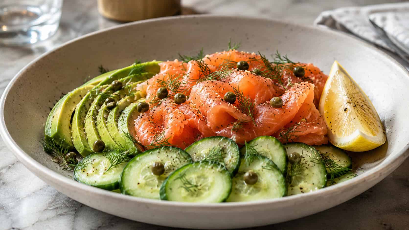 a fresh bowl of smoked salmon, sliced avocado, and cucumber with capers and dill in a wide horizontal shot, on a light ceramic plate with a lemon wedge, natural light, shallow depth of field, landscape orientation
