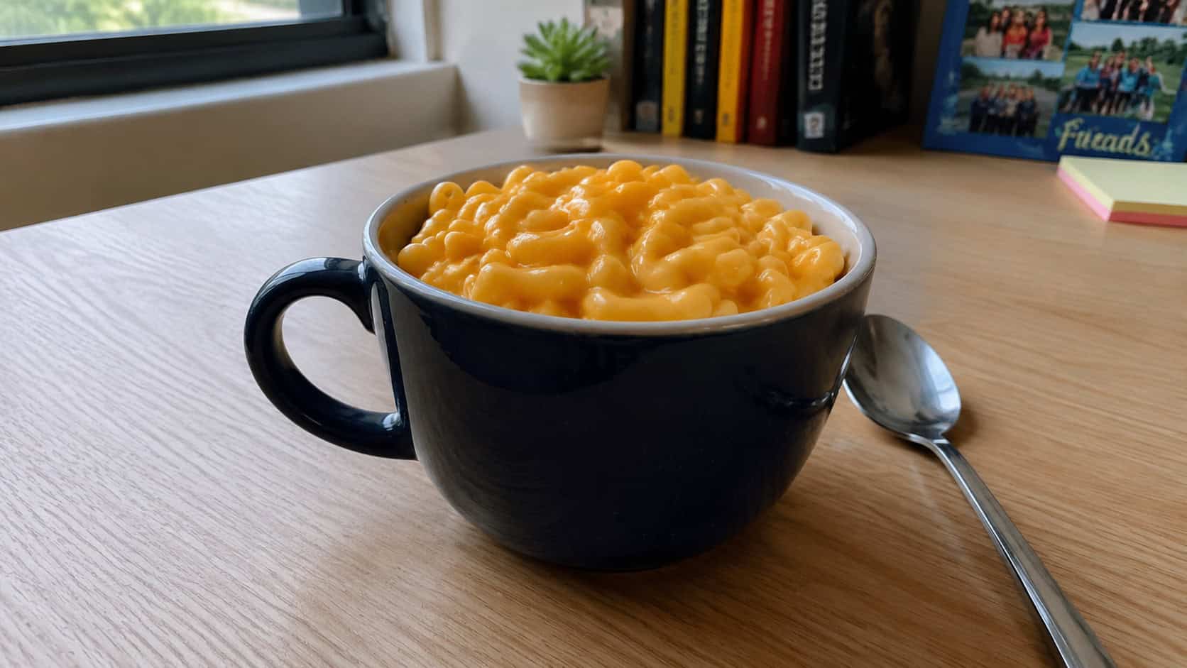 a mug of creamy golden macaroni and cheese in a wide horizontal shot, a spoon resting beside it on a marble countertop, a checkered napkin in the background, natural window light, shallow depth of field, landscape orientation
