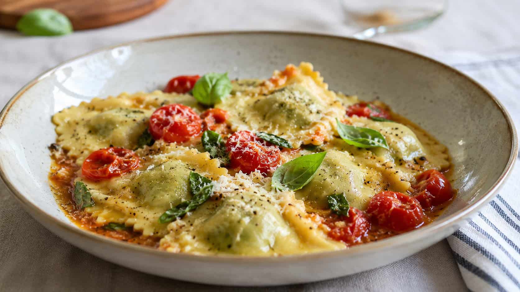 plump spinach ricotta ravioli in a buttery sauce with burst cherry tomatoes and fresh basil in a wide horizontal shot, served in a wide pasta bowl dusted with Parmesan on a linen tablecloth, natural light, shallow depth of field, landscape orientation
