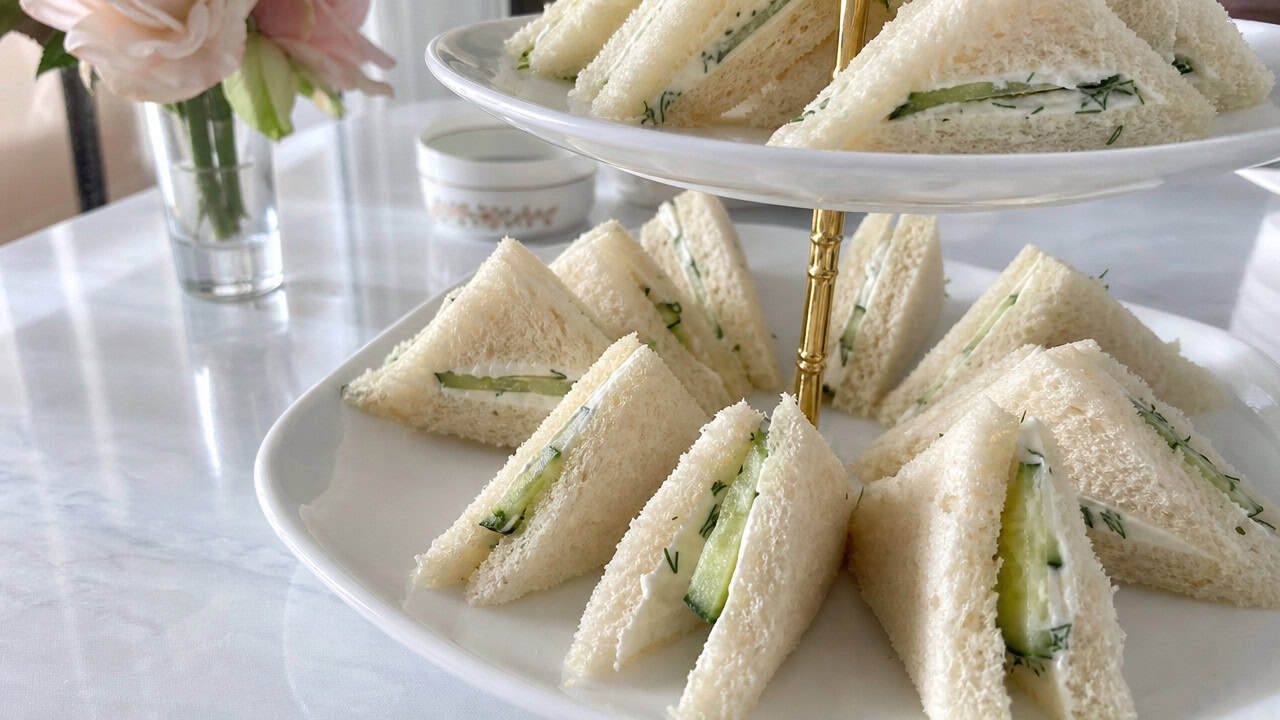 cucumber cream cheese tea sandwiches cut into triangles, arranged on a wide tiered plate on a bright table, natural light, shallow depth of field, landscape orientation