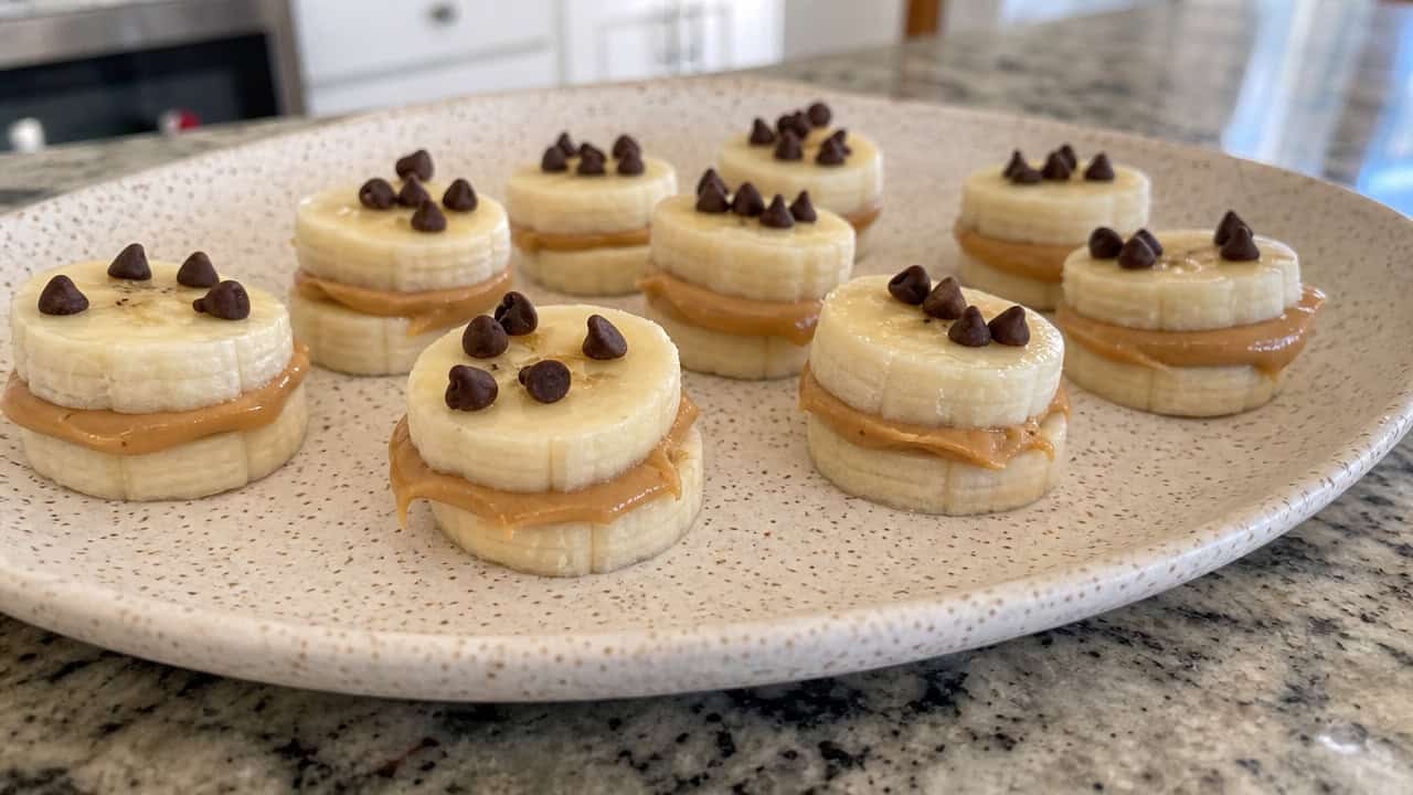 peanut butter banana bite sandwiches topped with mini chocolate chips, spread across a wide speckled plate on a kitchen counter, natural light, shallow depth of field, landscape orientation