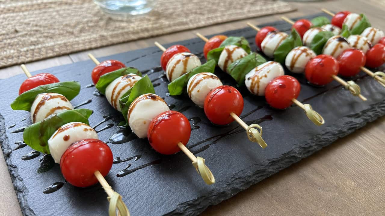 caprese skewers with cherry tomatoes, mozzarella, and basil drizzled with balsamic, lined up on a wide slate board on a table, natural light, shallow depth of field, landscape orientation