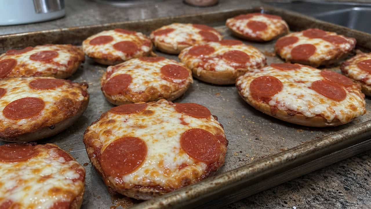 mini pizza bagels with bubbly melted cheese and pepperoni arranged on a wide baking tray on a counter, natural light, shallow depth of field, landscape orientation